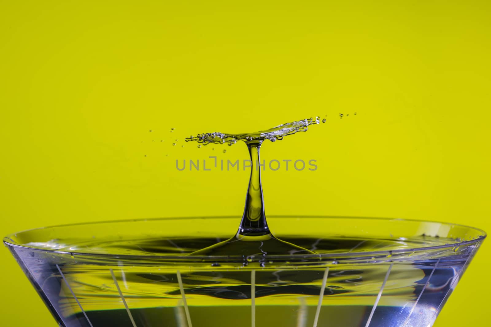 A falling drop collides with a rising splash column over a martini glass, creating a flat disk of radiating spray.