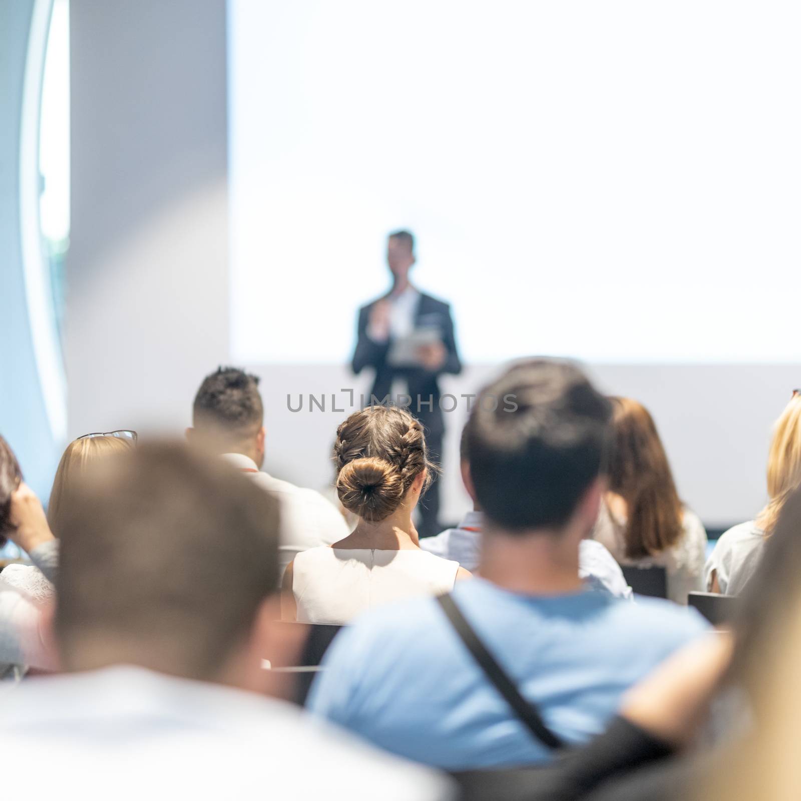 Male speaker giving a talk in conference hall at business event. Audience at the conference hall. Business and Entrepreneurship concept. Focus on unrecognizable people in audience.