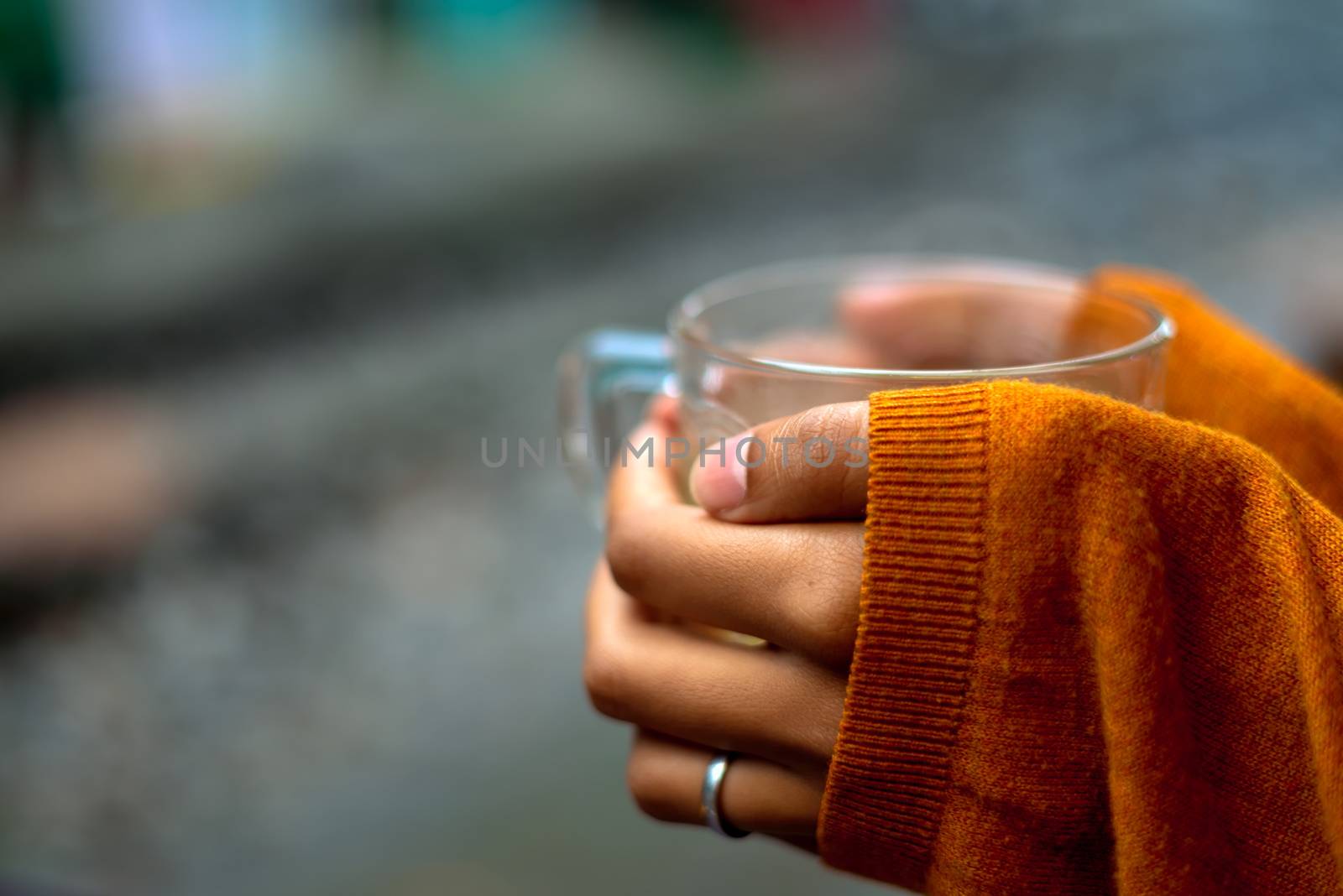 holding a cup of tea by rails waiting for the train with orange pullover covering hands by half