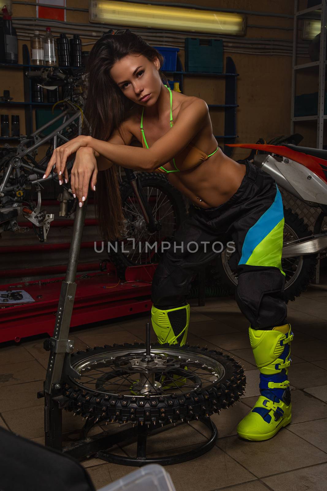 Sexy girl in garage with motorcycles posing with studded tires