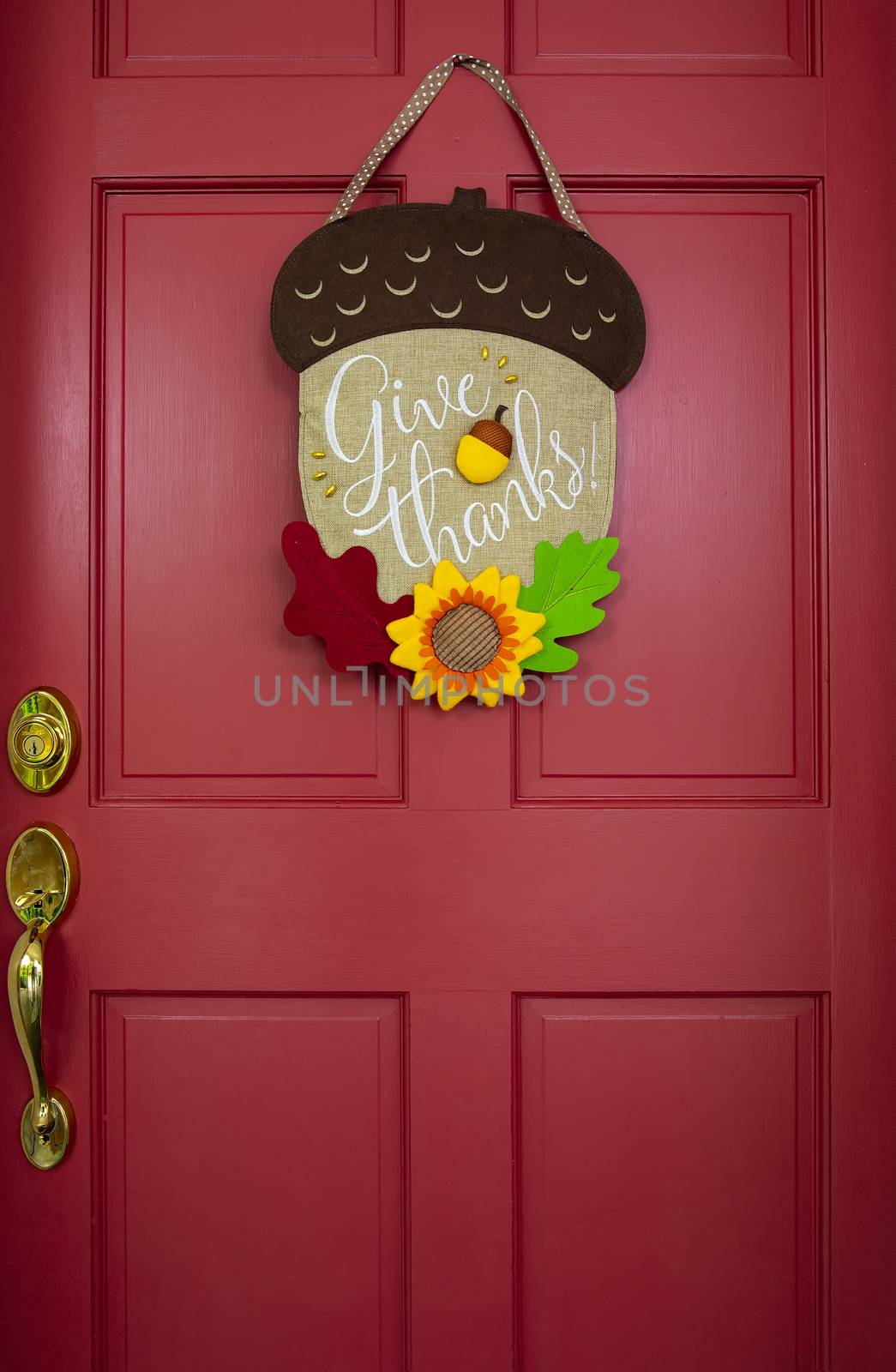 Fall-themed decoration hangs on red entrance door with brass handle.