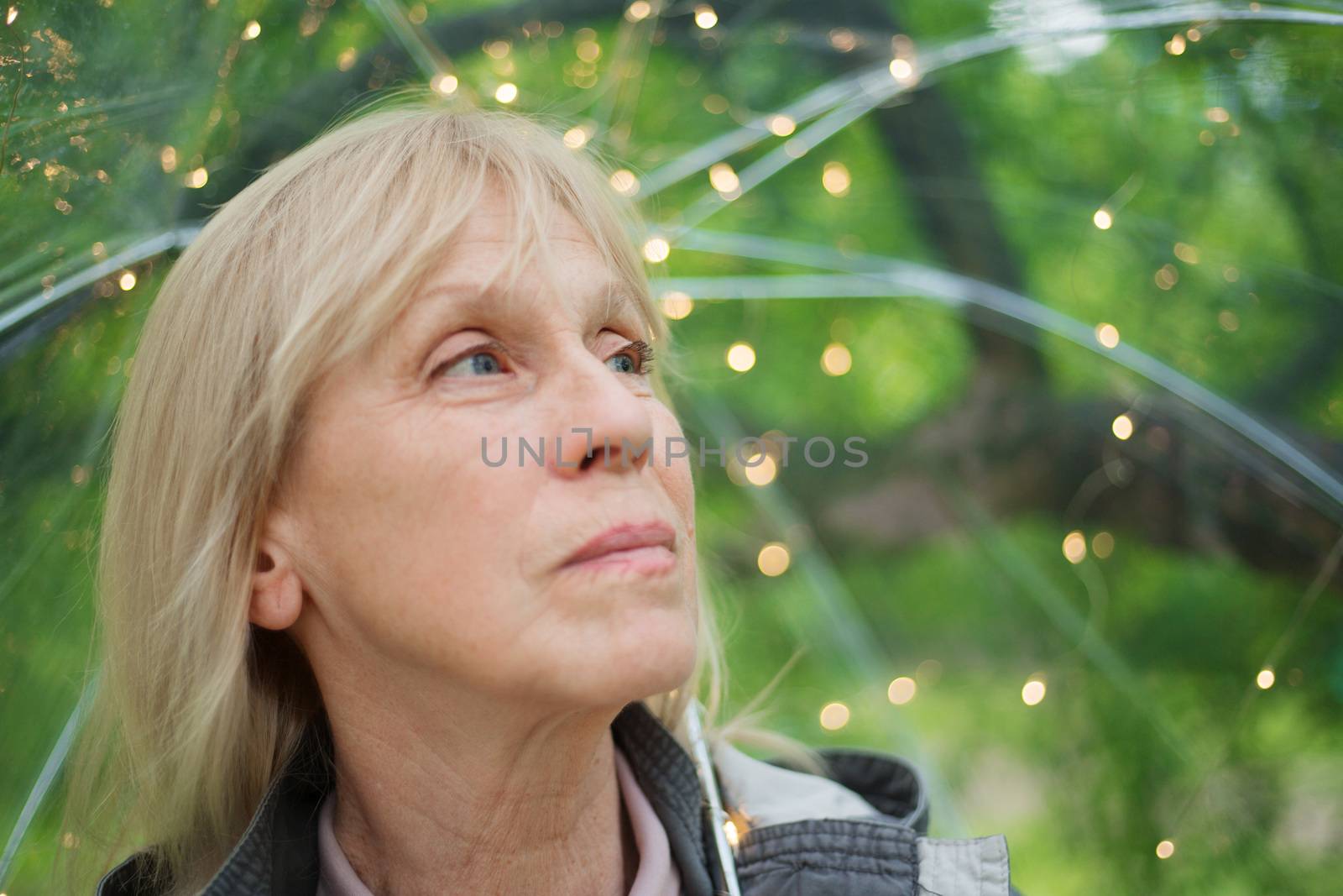 Portrait of beautiful senior woman with transparent umbrella with light bokeh background