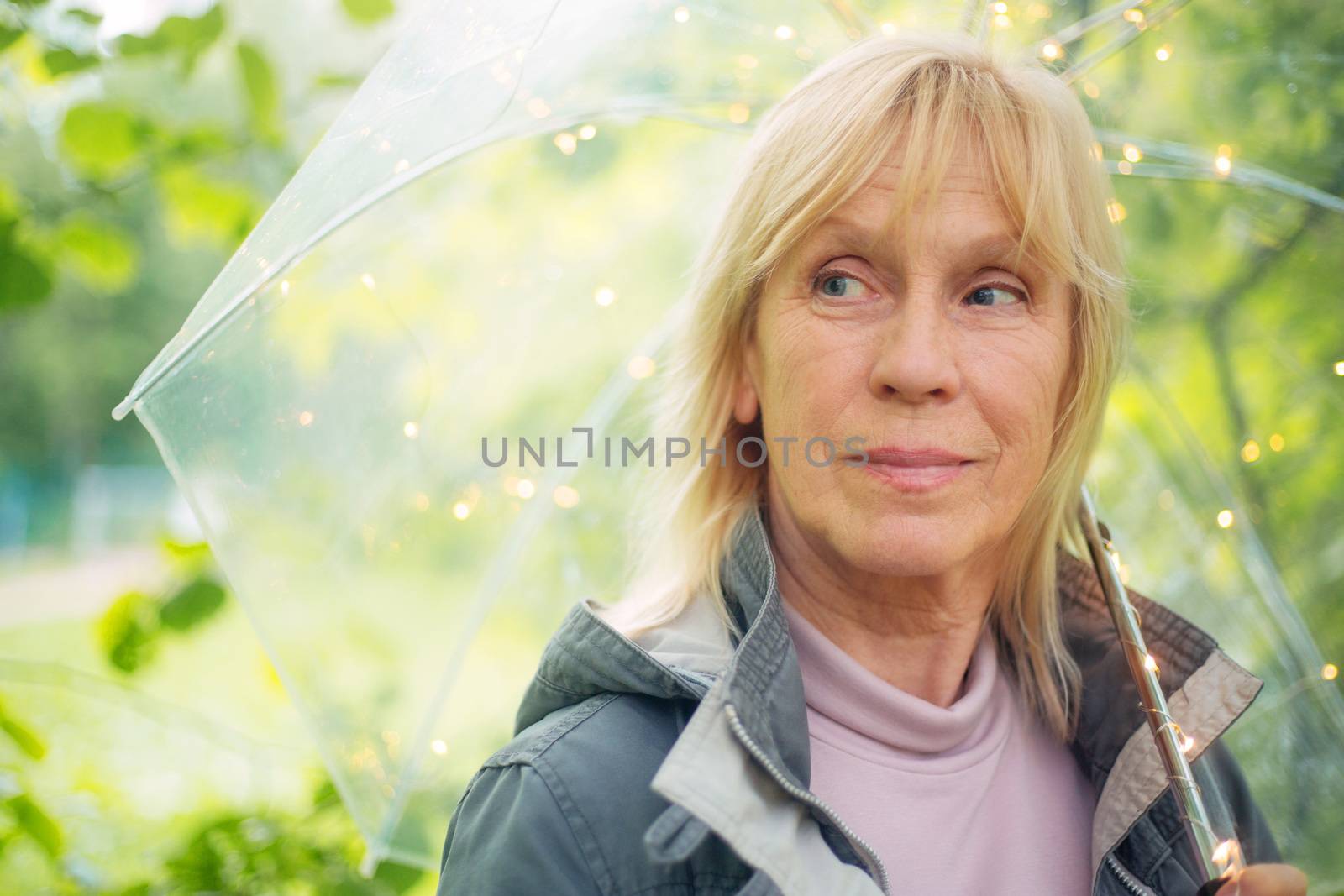Portrait of beautiful senior woman with transparent umbrella with light bokeh background