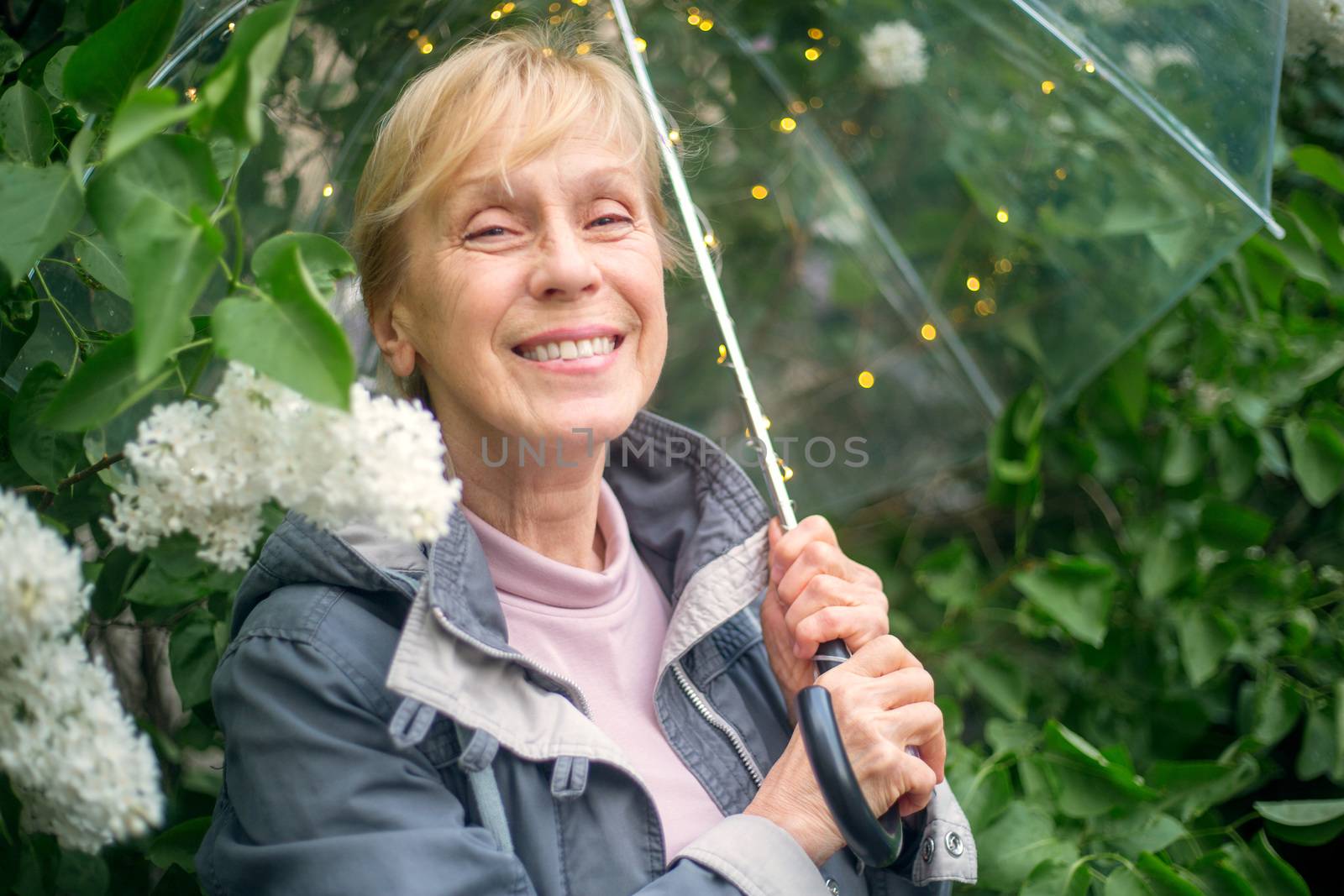 Portrait of beautiful senior woman with transparent umbrella with light bokeh background