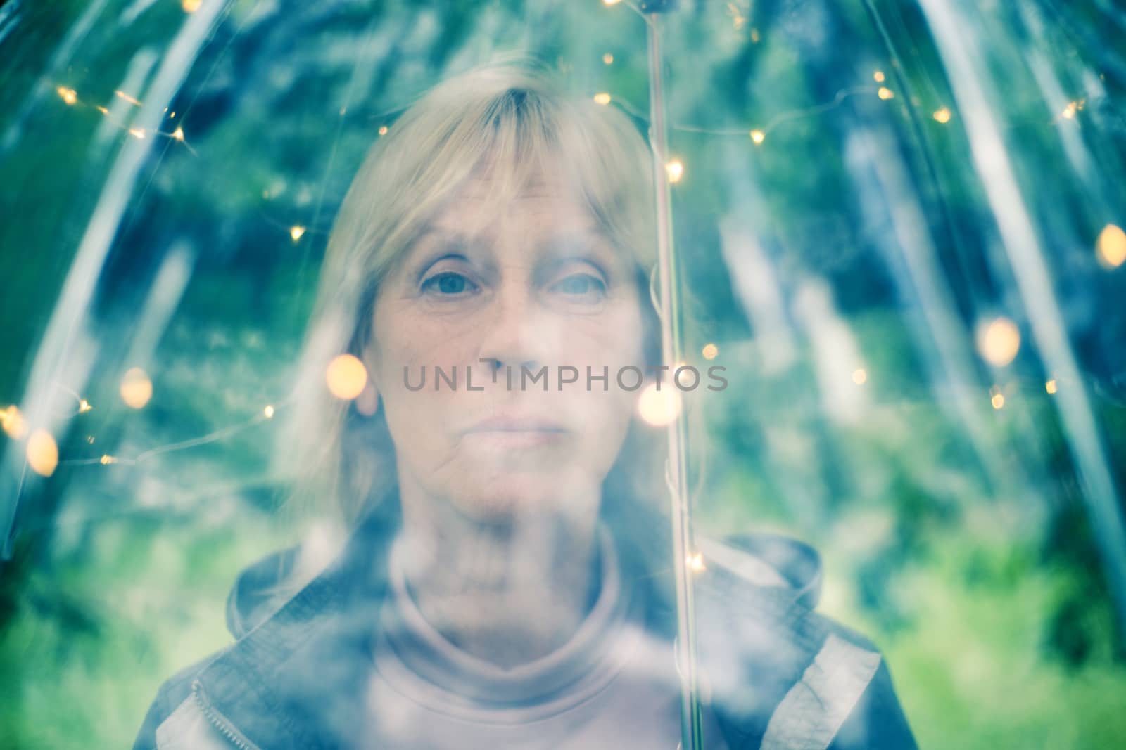 Portrait of beautiful senior woman with transparent umbrella with light bokeh background