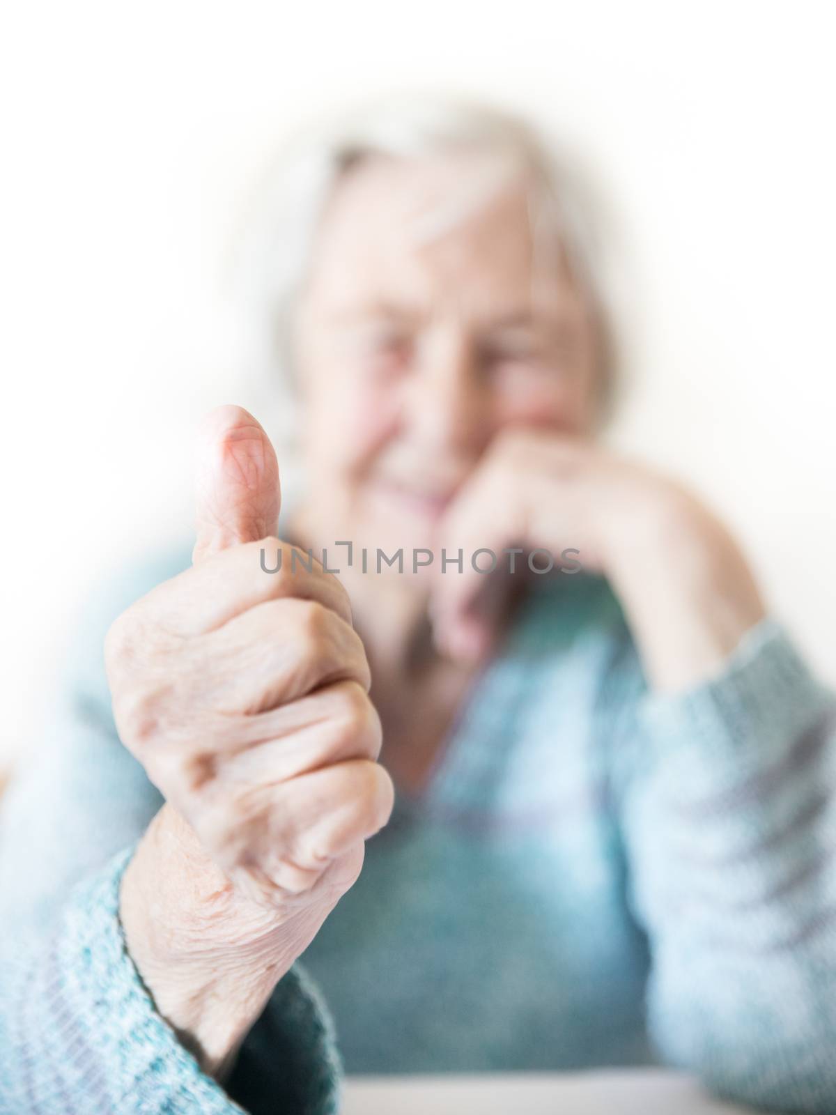 Content 96 years old elderly woman giving a thumb up and looking at camera. Focus on the thumb up, face out of focus. Old age and the quality of life concept.