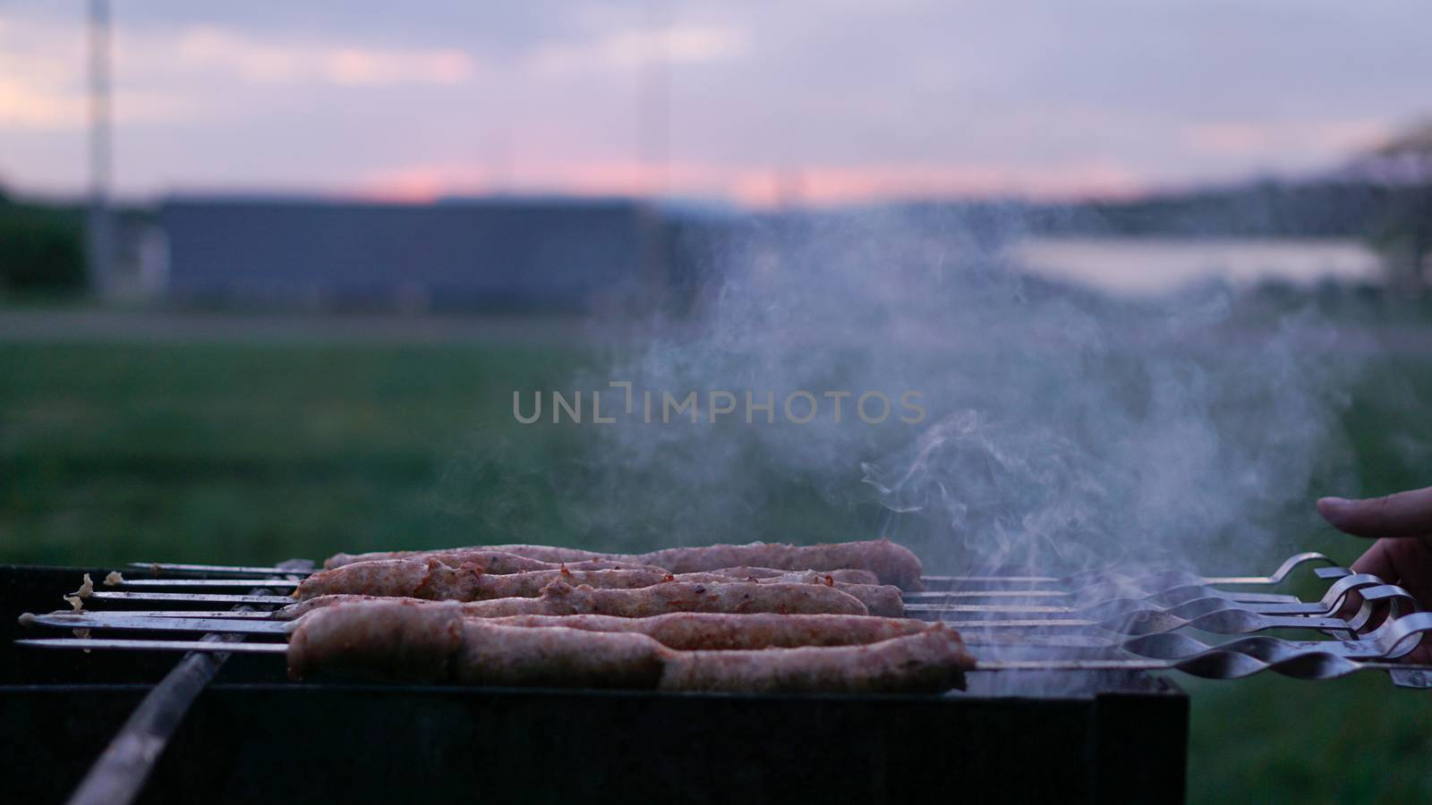 Grilling sausages at sunset outdoors gathering with friends and family. Sunner time