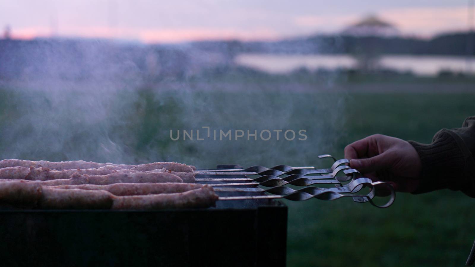 Grilling sausages at sunset outdoors gathering with friends and family. Sunner time