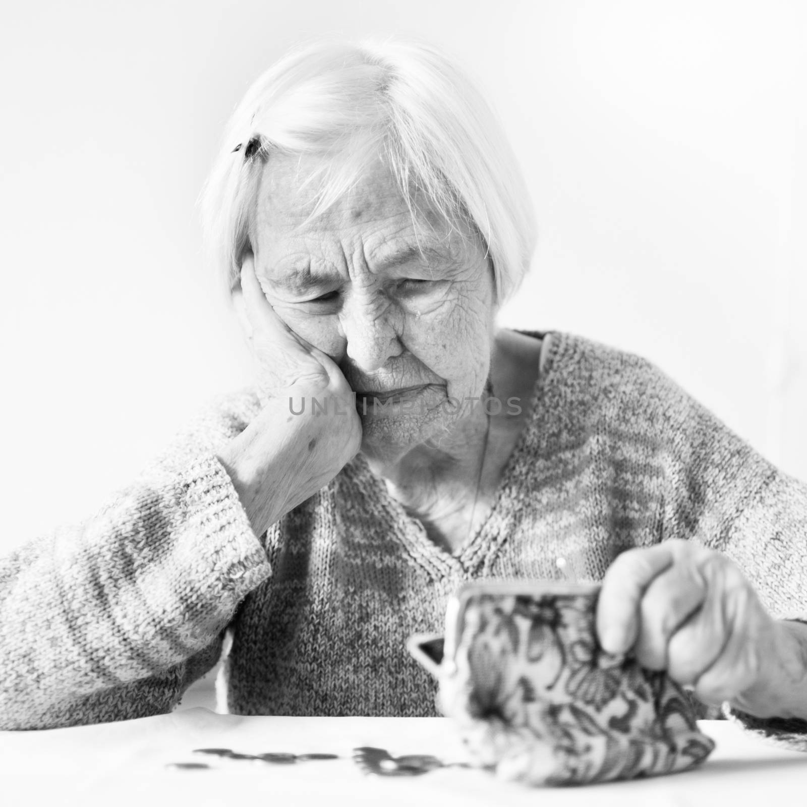 Concerned elderly 96 years old woman sitting at table at home and counting remaining coins from pension in her wallet after paying bills. Unsustainability of social transfers and pension system.