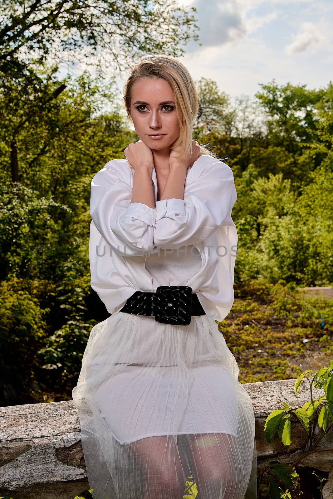 Young blonde woman in white skirt and shirt in the old sunny summer city park. Fashion woman. Young woman's modern portrait.