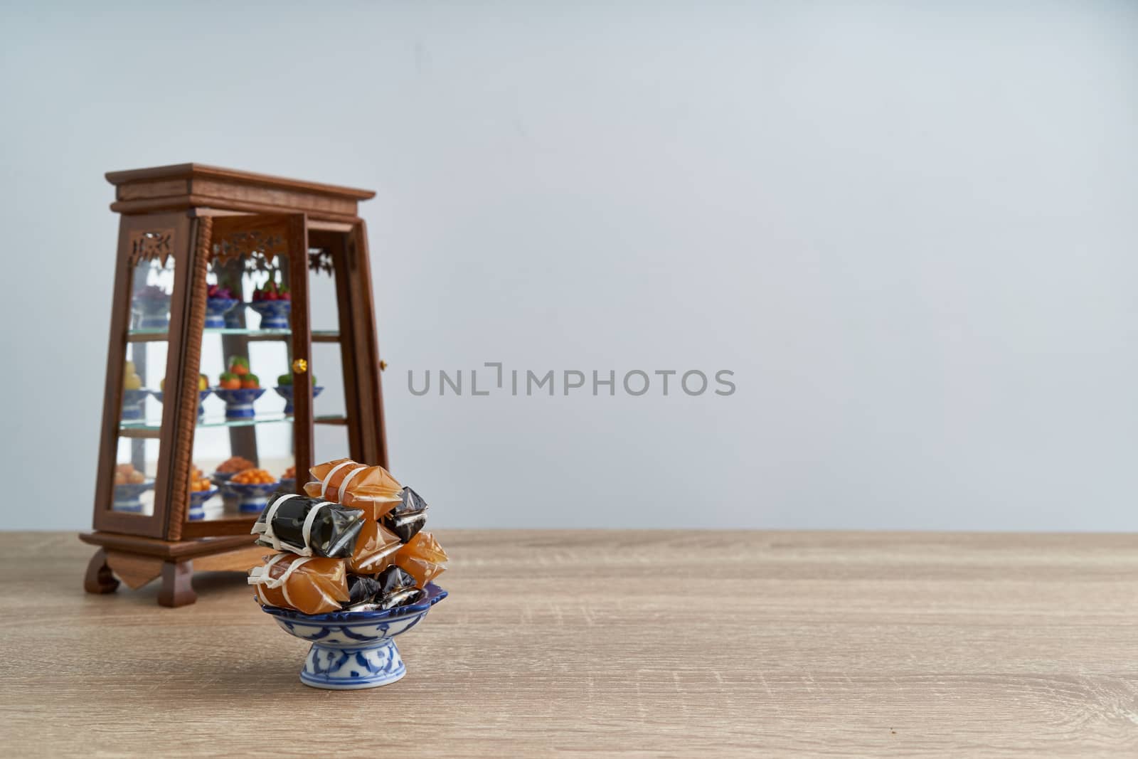 Stack of Thai caramel or Kalamare with sesame on pedestal tray have blur cabinet with Thai dessert place on wood table with white background and copy space. Sweet and gummy snack of Thai food.