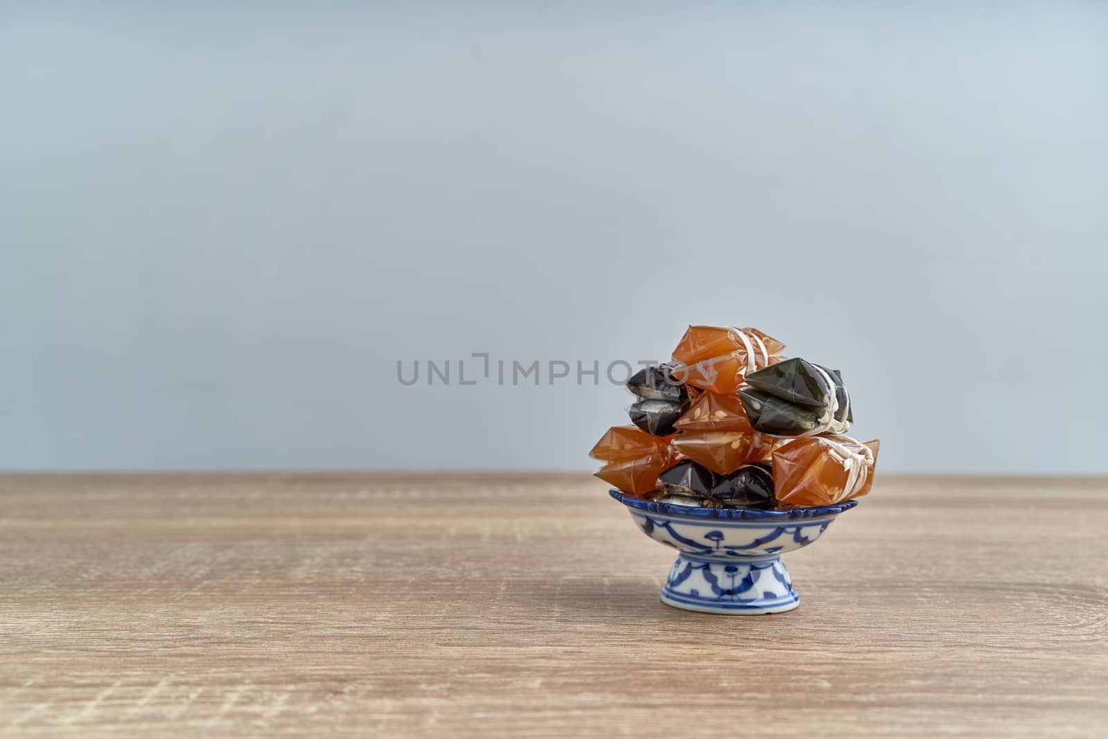 Stack of Thai caramel or Kalamare with sesame on pedestal tray place on wood table with white background and copy space. Sweet and gummy snack of Thai food.