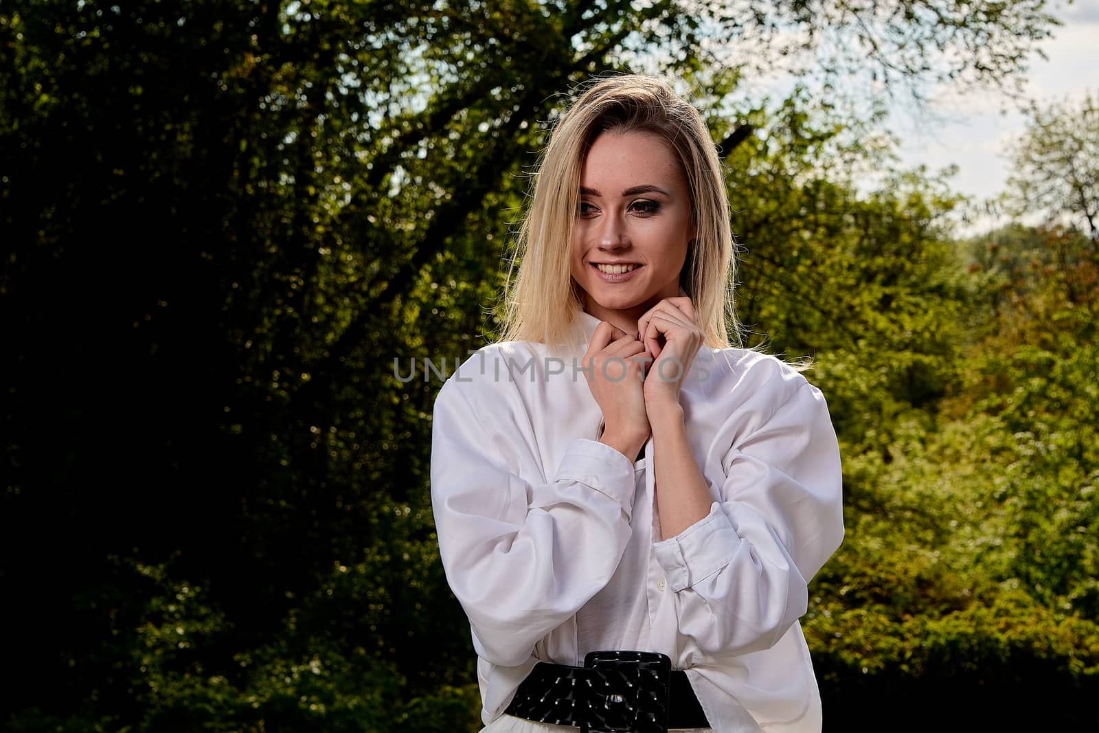 Young blonde woman in white skirt and shirt in the old sunny summer city park. Fashion woman. Young woman's modern portrait.