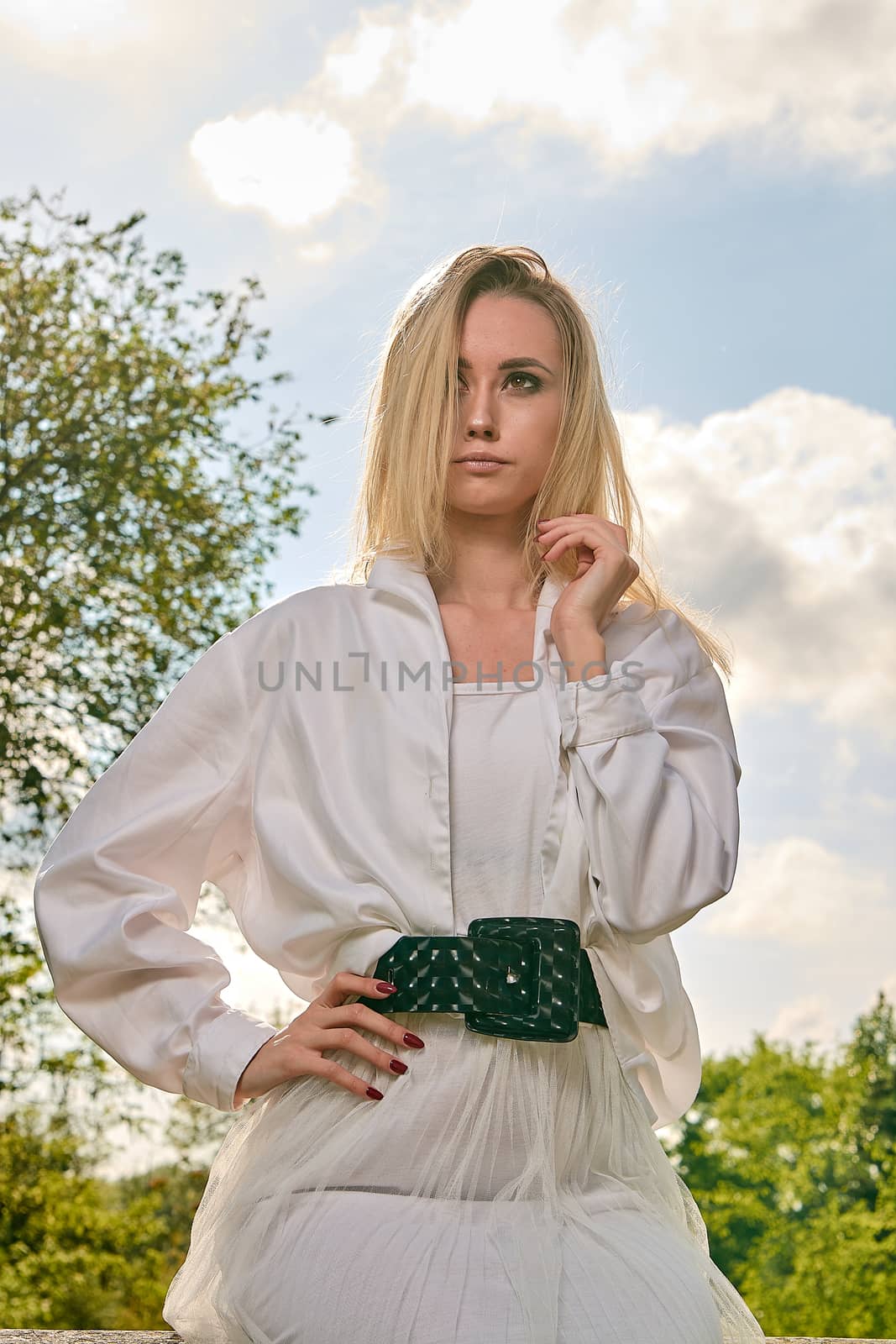 Young blonde woman in white skirt and shirt in the old sunny summer city park. Fashion woman. Young woman's modern portrait.