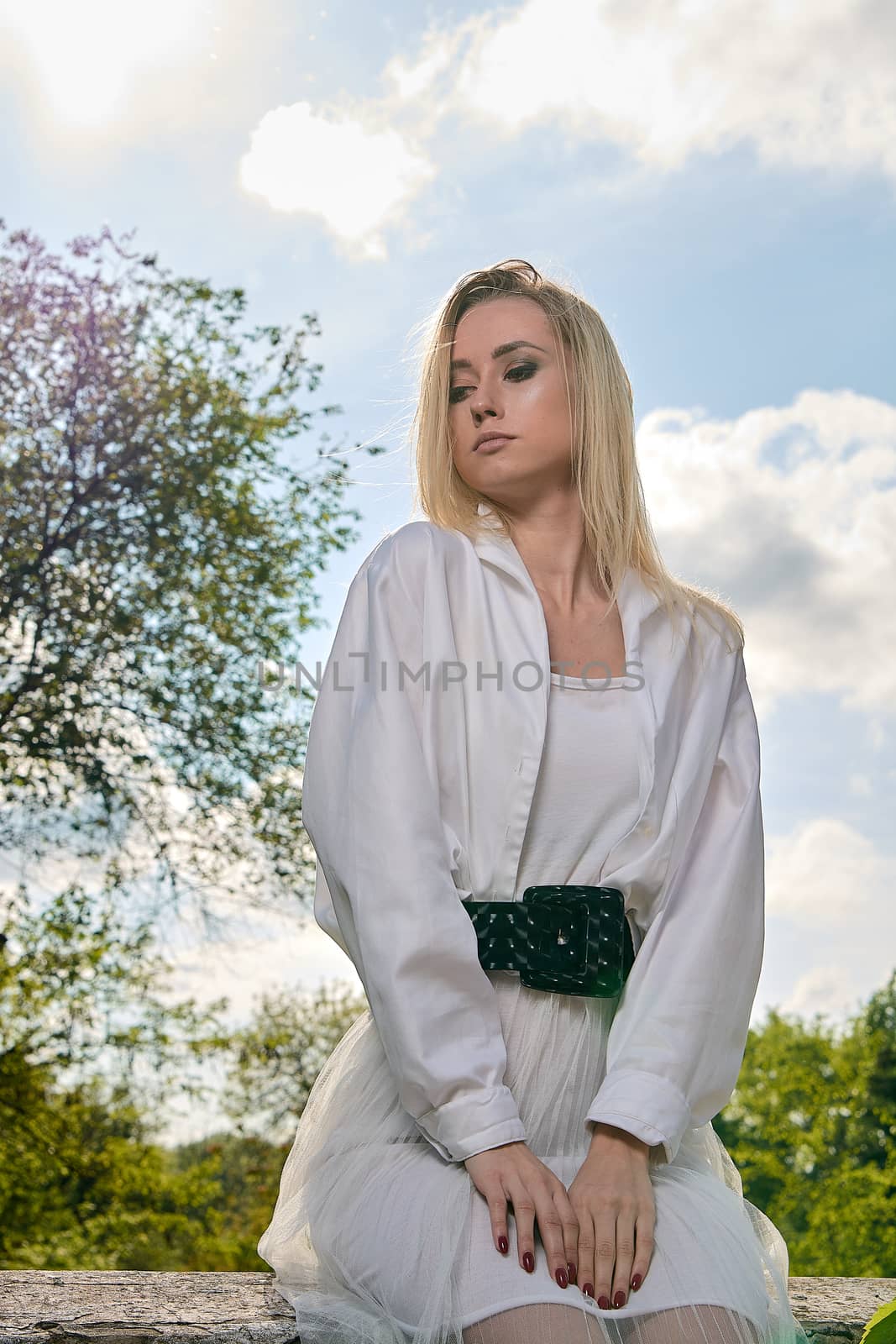 Young blonde woman in white skirt and shirt in the old sunny summer city park. Fashion woman. Young woman's modern portrait.