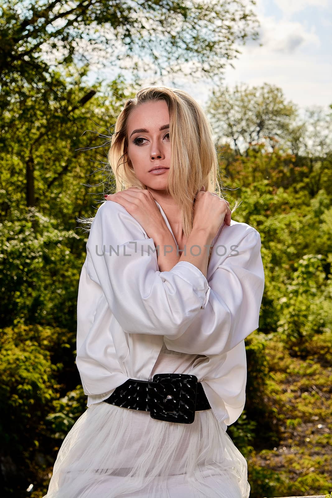 Young blonde woman in white skirt and shirt in the old sunny summer city park. Fashion woman. Young woman's modern portrait.