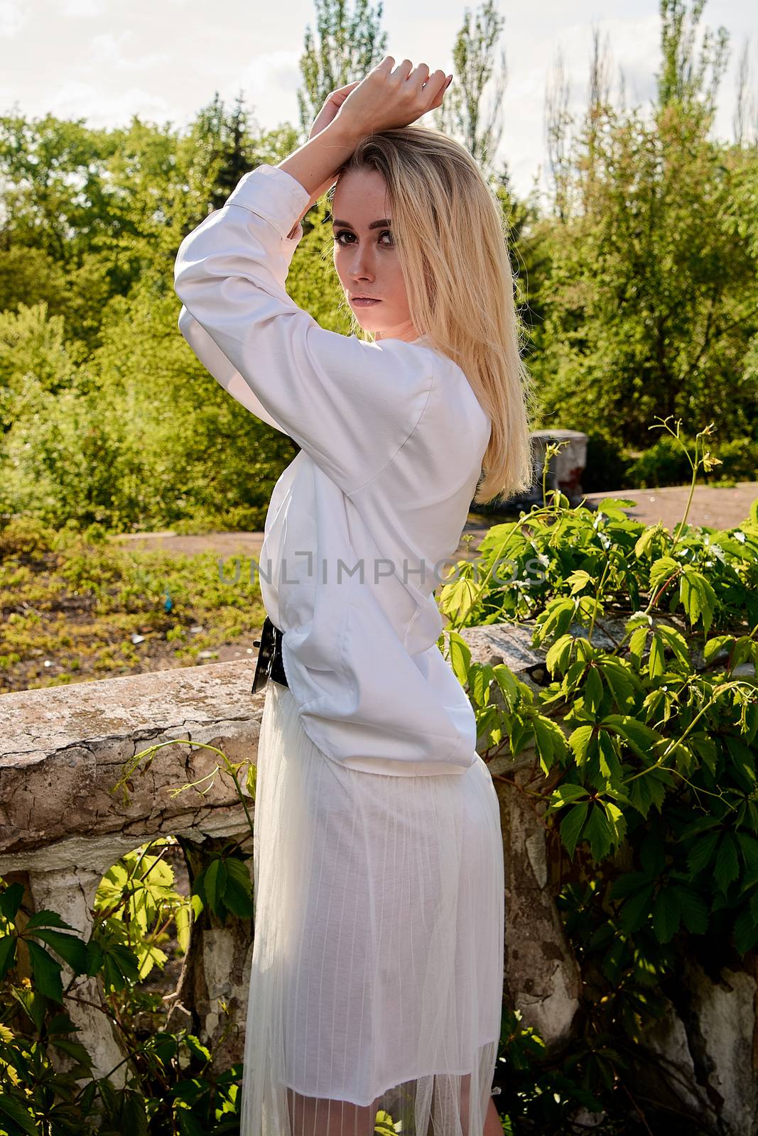 Young blonde woman in white skirt and shirt in the old sunny summer city park. Fashion woman. Young woman's modern portrait.