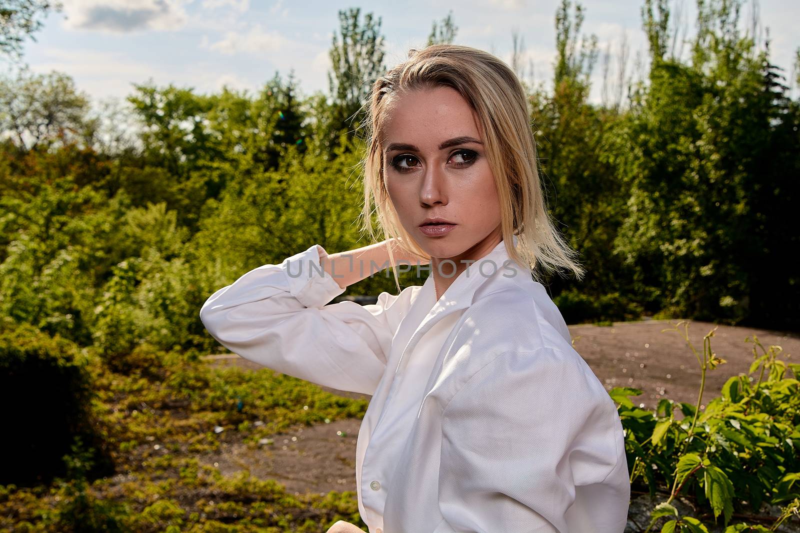 Young blonde woman in white skirt and shirt in the old sunny summer city park. Fashion woman. Young woman's modern portrait.