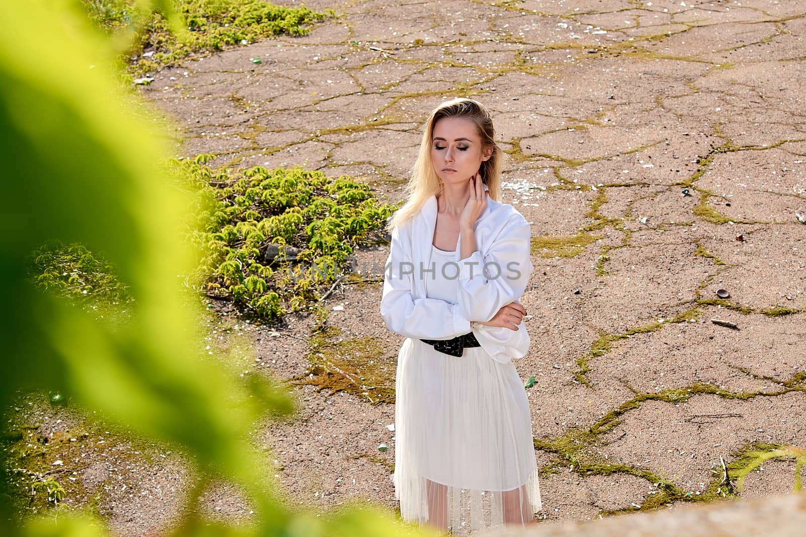 Young blonde woman in white skirt and shirt in the old sunny summer city park. Fashion woman. Young woman's modern portrait.