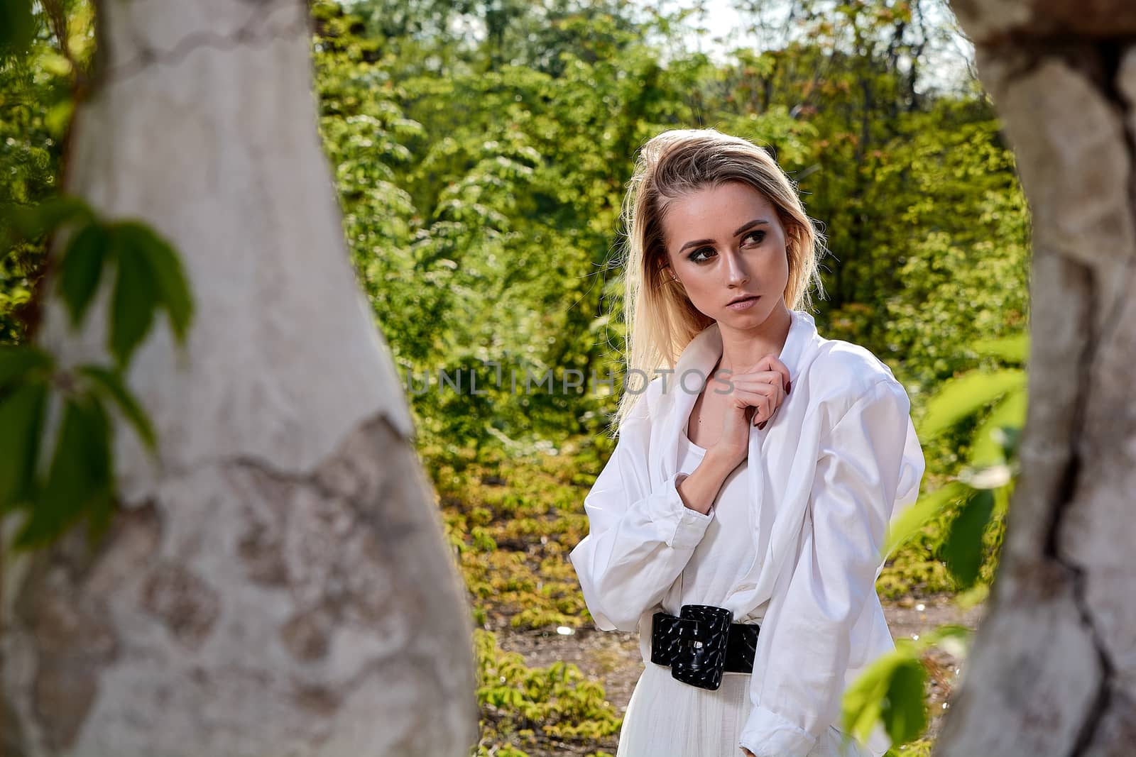 Young blonde woman in white skirt and shirt in the old sunny summer city park. Fashion woman. Young woman's modern portrait.