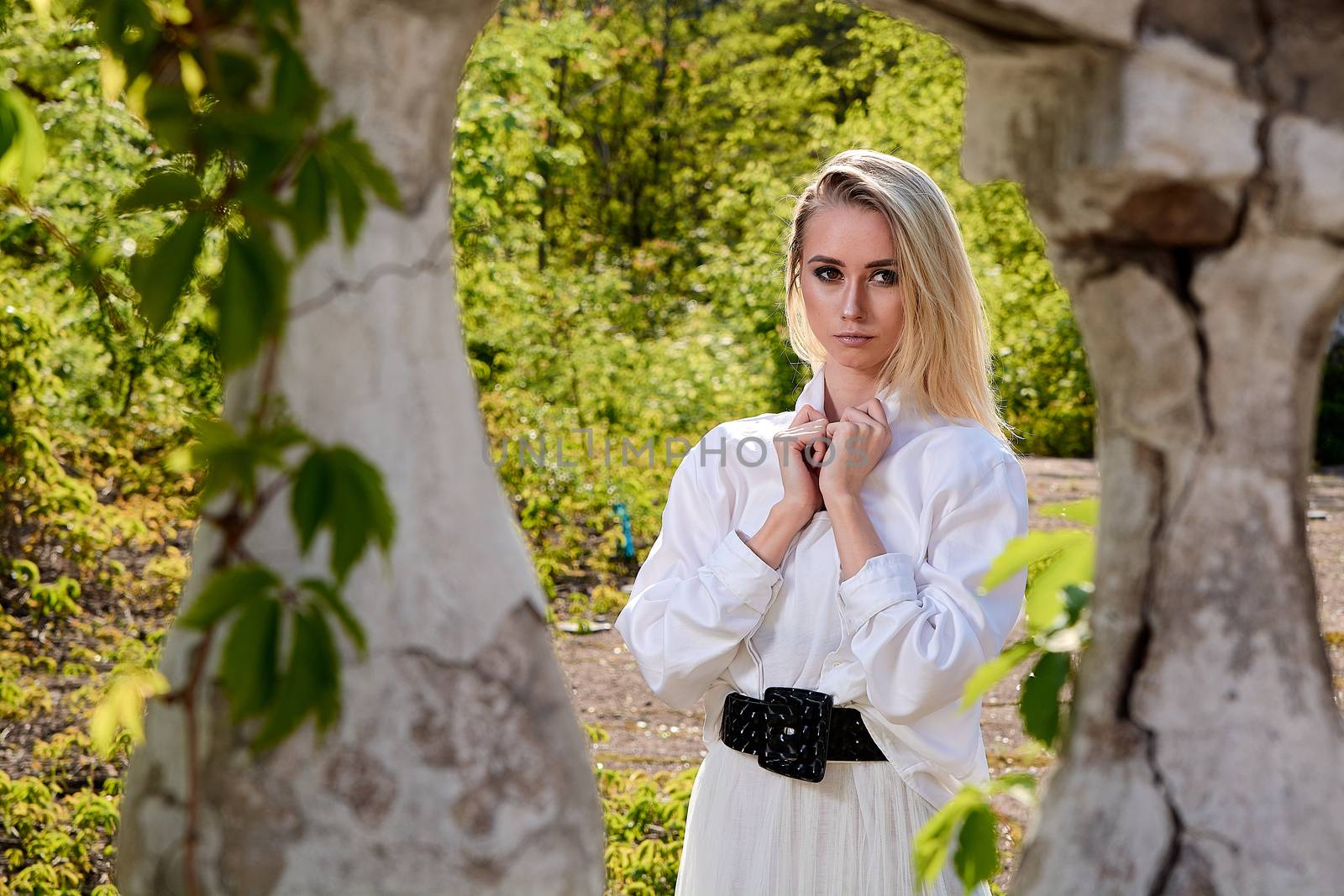 Young blonde woman in white skirt and shirt in the old sunny summer city park. Fashion woman. Young woman's modern portrait.