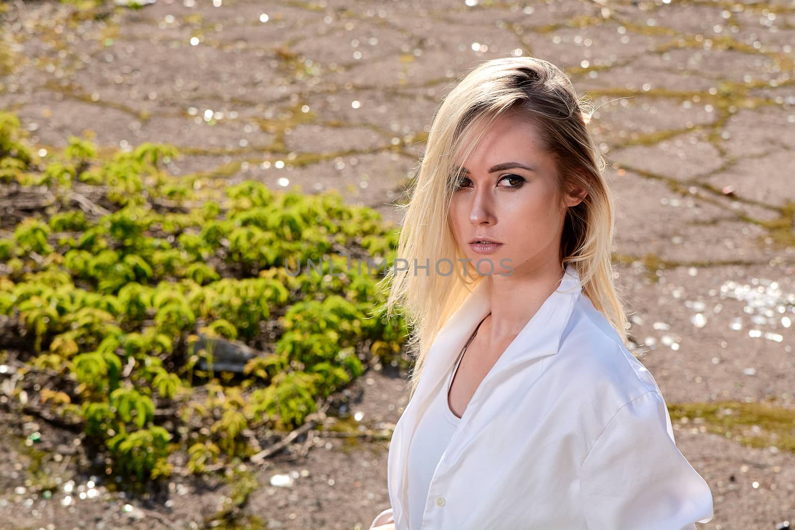 Young blonde woman in white skirt and shirt in the old sunny summer city park. Fashion woman. Young woman's modern portrait.