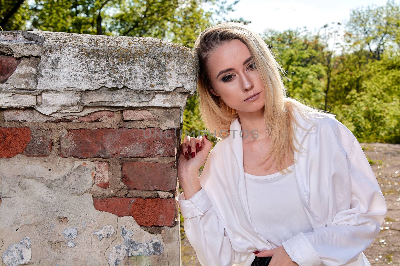 Young blonde woman in white skirt and shirt in the old sunny summer city park. Fashion woman. Young woman's modern portrait.