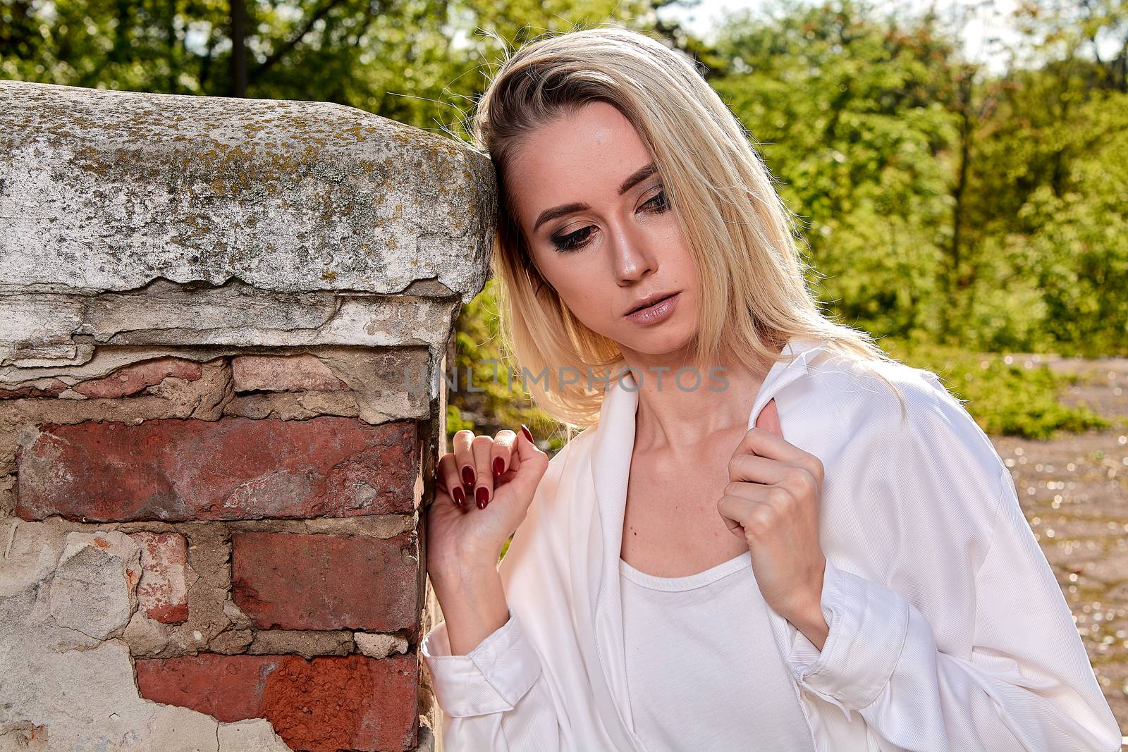 Young blonde woman in white skirt and shirt in the old sunny summer city park. Fashion woman. Young woman's modern portrait.