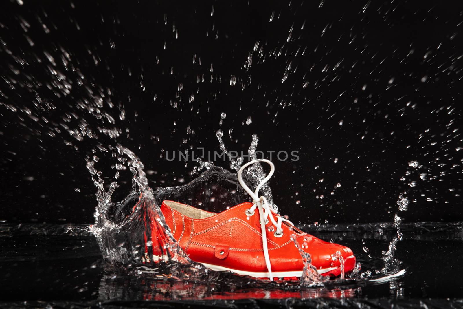 Red shoe falling in a water with splashes on a black background
