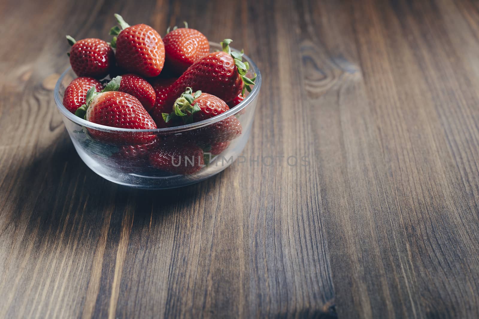 Heap of fresh strawberries in glass bowl on rustic wooden background, healthy sweet food, vitamins and fruity concept. Copy space for text