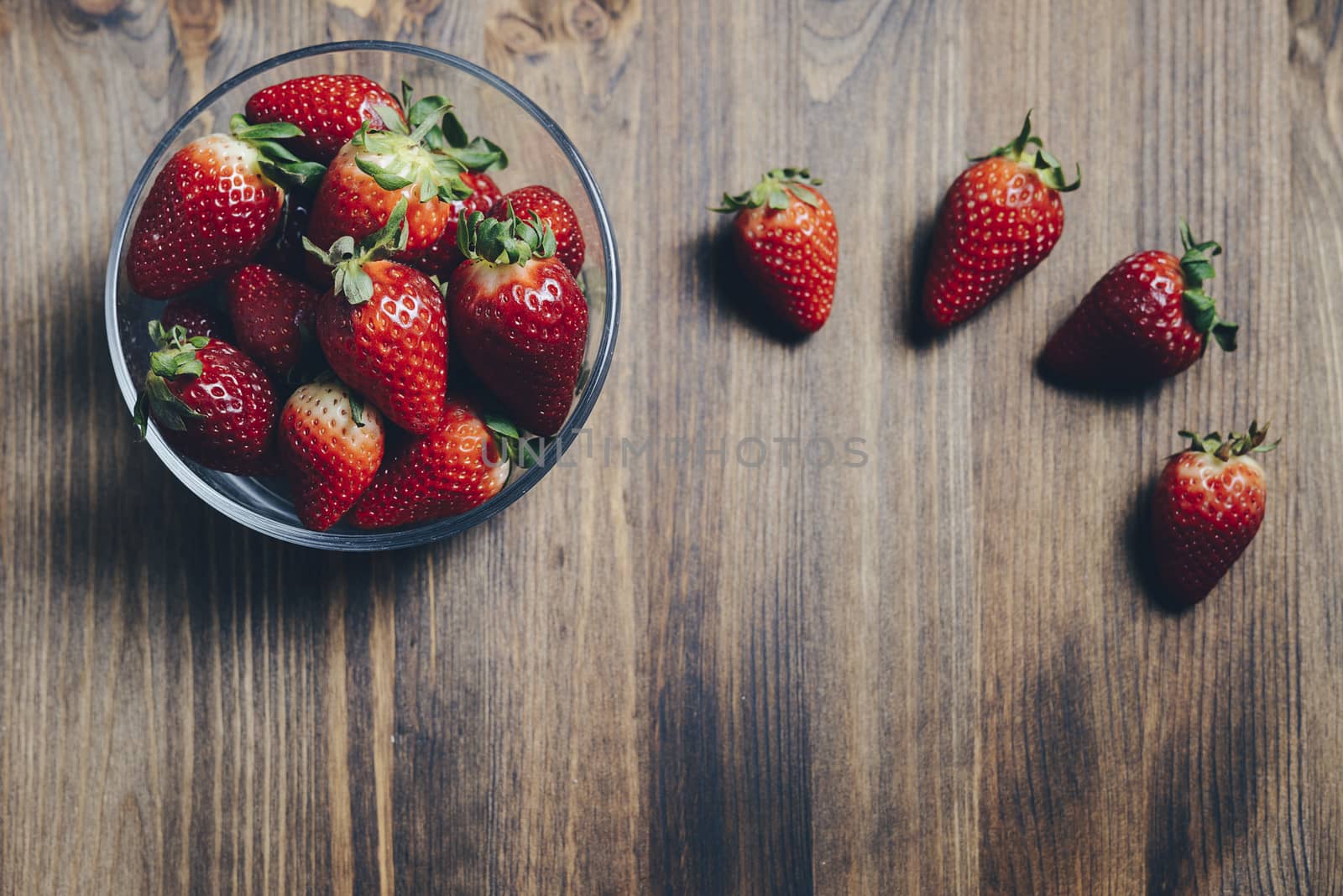 Juicy fresh strawberries in a glass bowl on old wooden background, healthy sweet food, vitamins and fruity concept. Top view, copy space for text