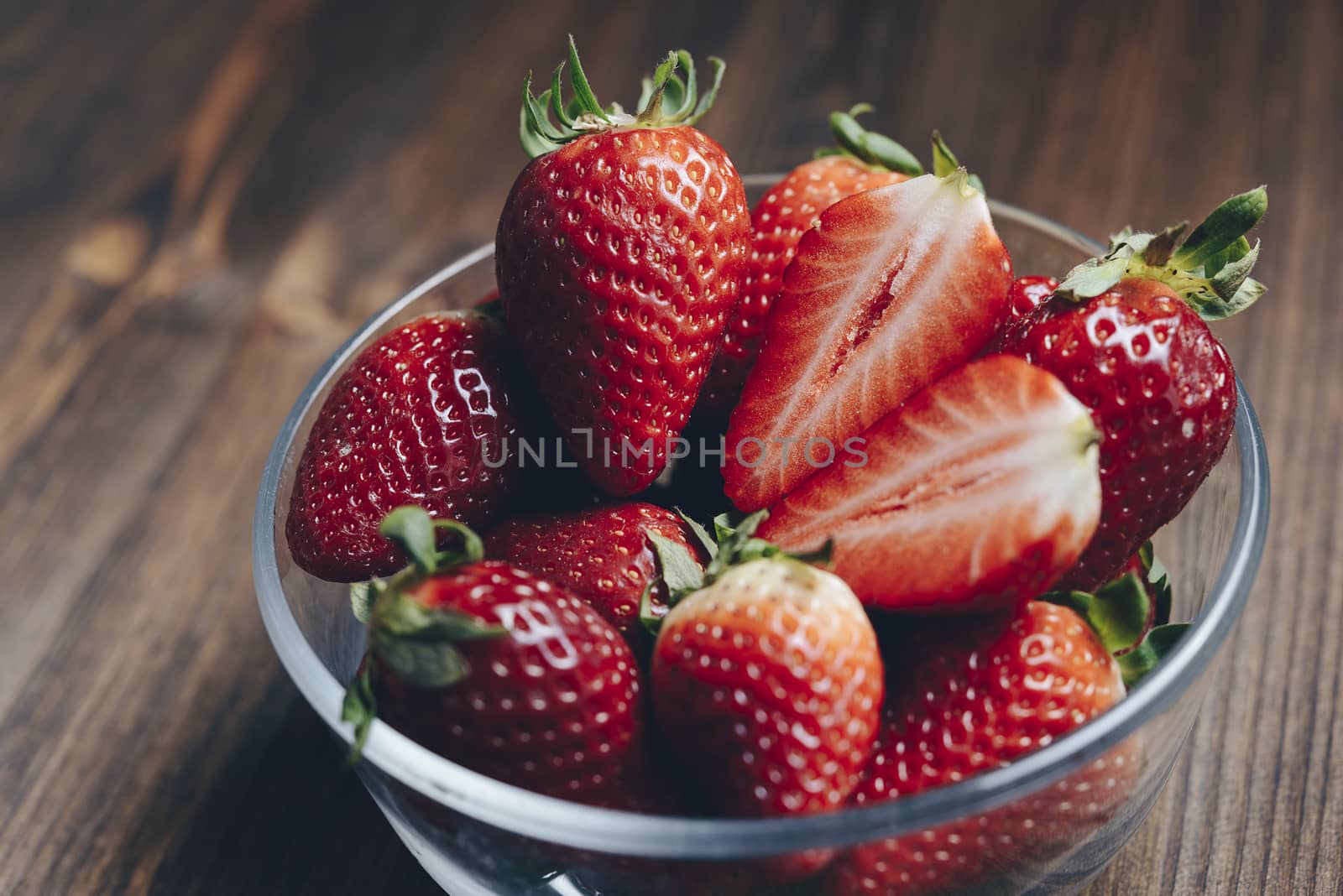 Fresh strawberries in a glass bowl on wooden table in rustic style, healthy sweet food, vitamins and fruity concept