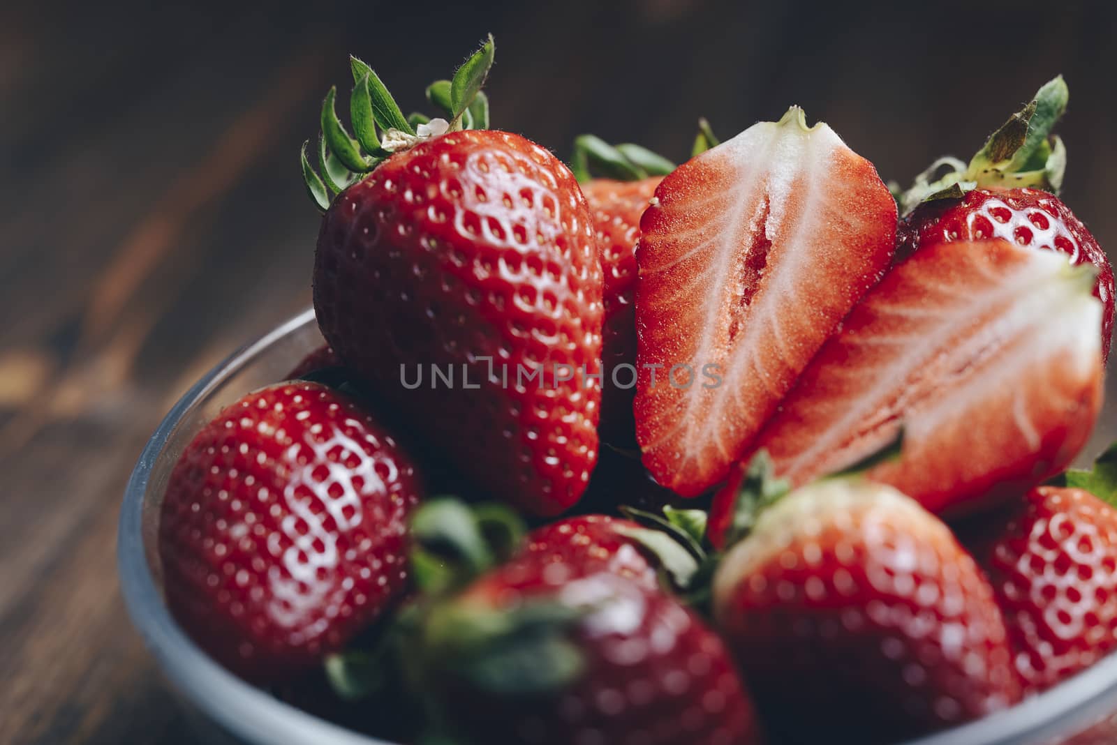 Fresh strawberries in a glass bowl on wooden background in rustic style, healthy sweet food, vitamins and fruity concept. Selective focus