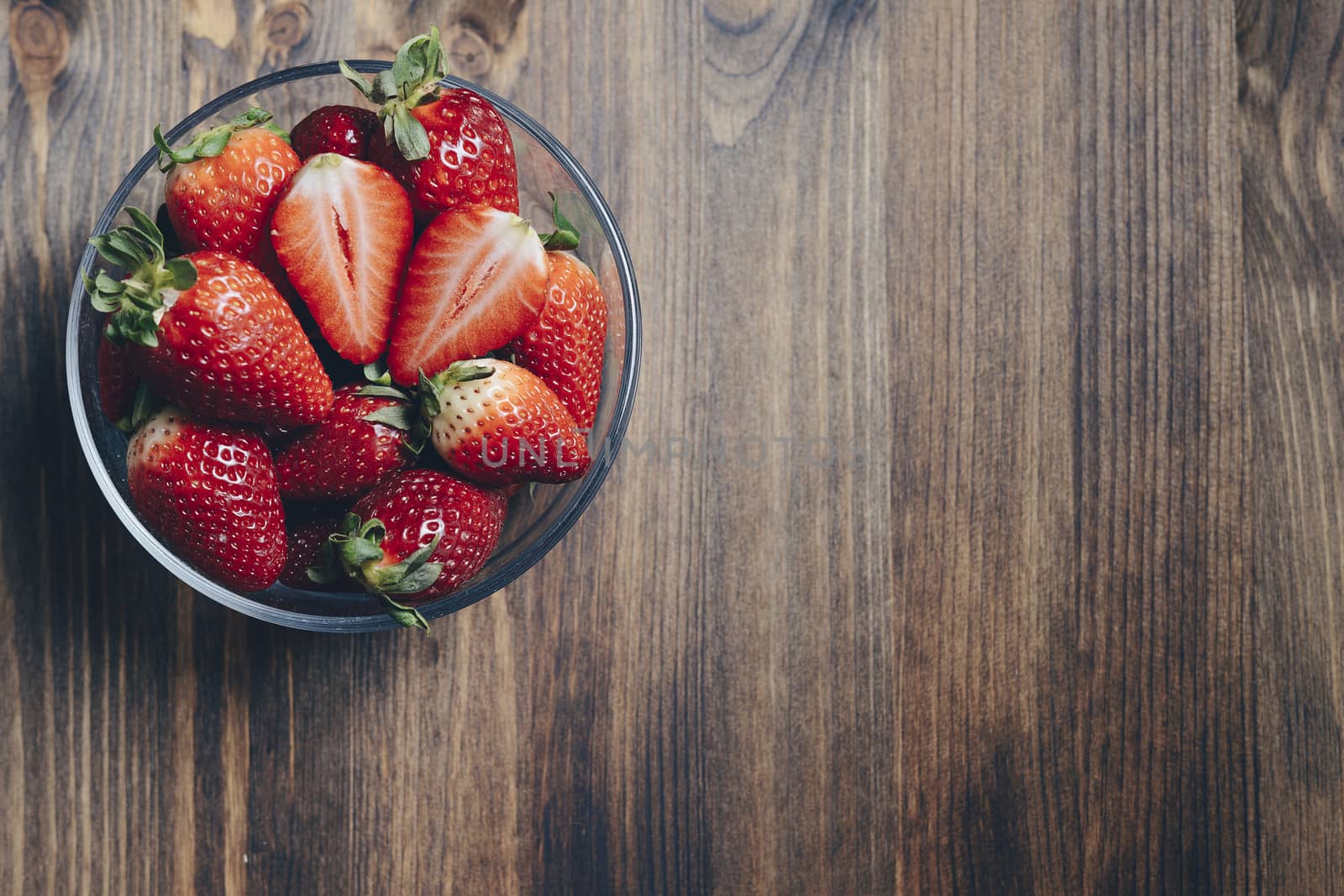 Fresh strawberries in a glass bowl on wooden background in rustic style, healthy sweet food, vitamins and fruity concept. Top view, copy space for text