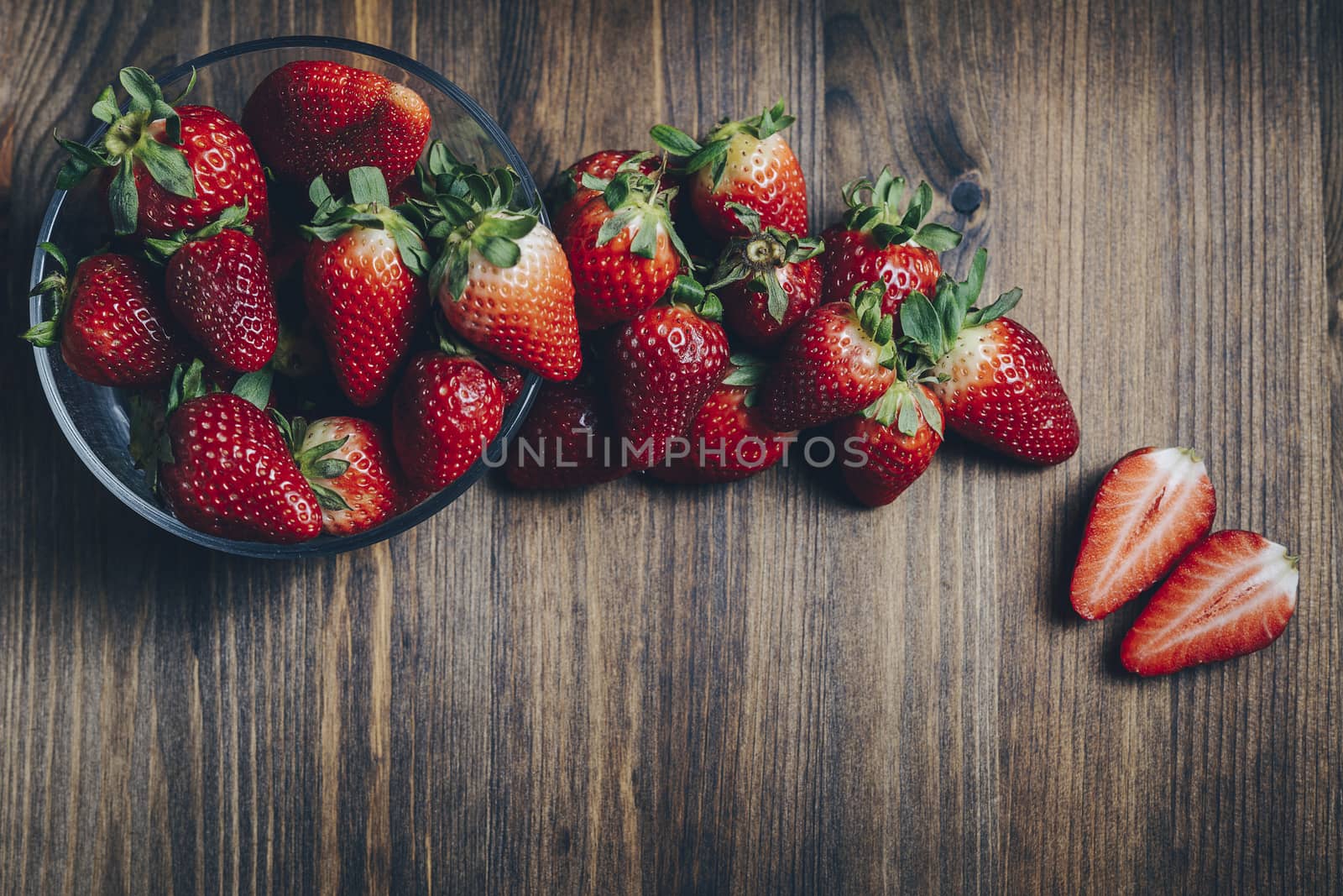 Fresh and juicy strawberries in a glass bowl on wooden table in rustic style, healthy sweet food, vitamins and fruity concept. Top view, copy space for text