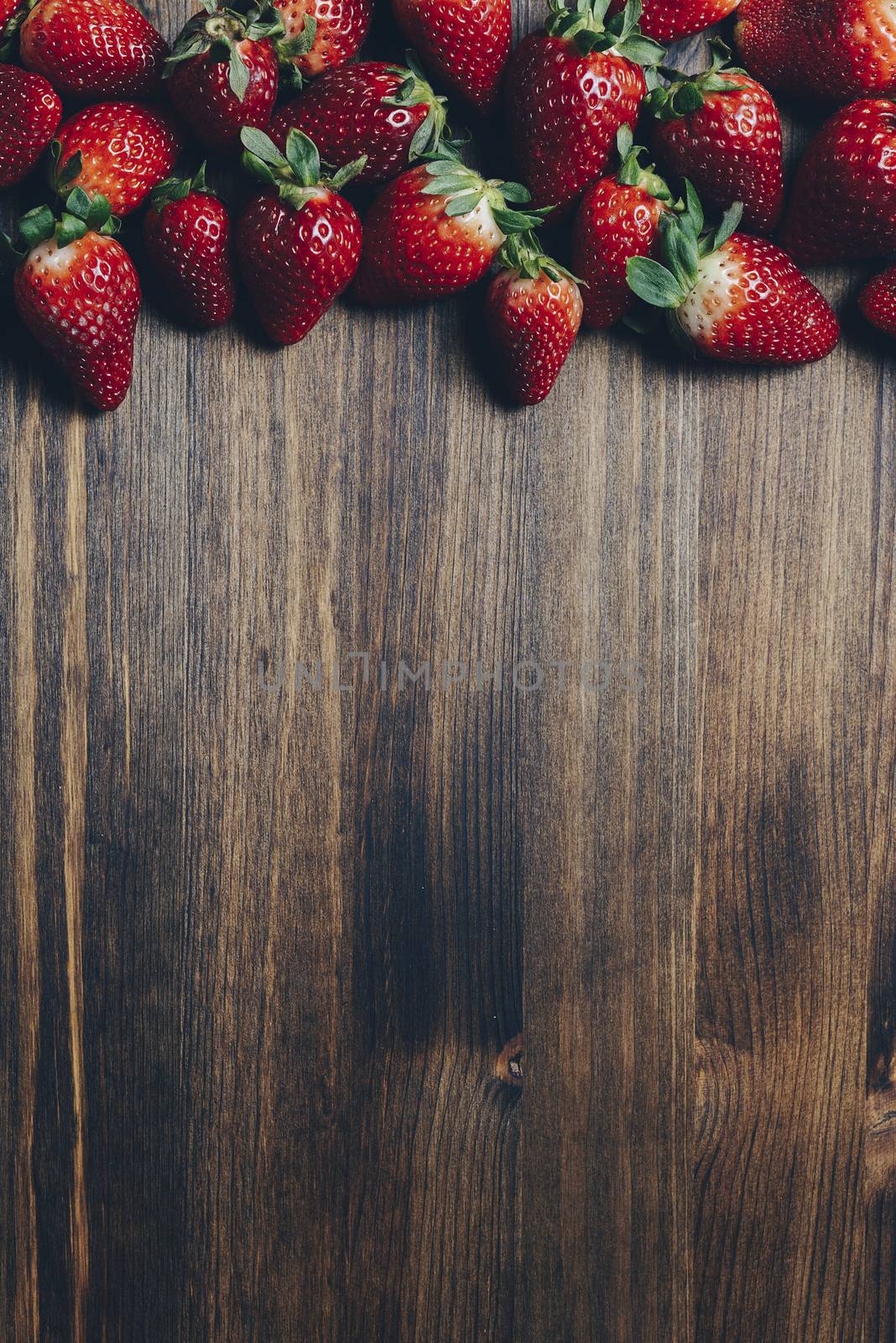 Fresh and juicy strawberries on wooden background in rustic style, healthy sweet food, vitamins and fruity concept. Vertical photo, top view, copy space for text