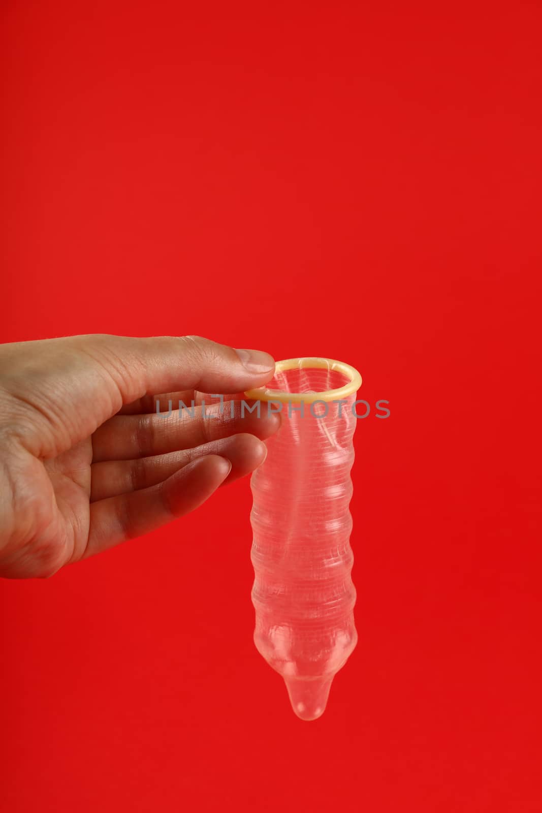 Close up woman hand holding one open latex condom over red background with copy space, low angle side view