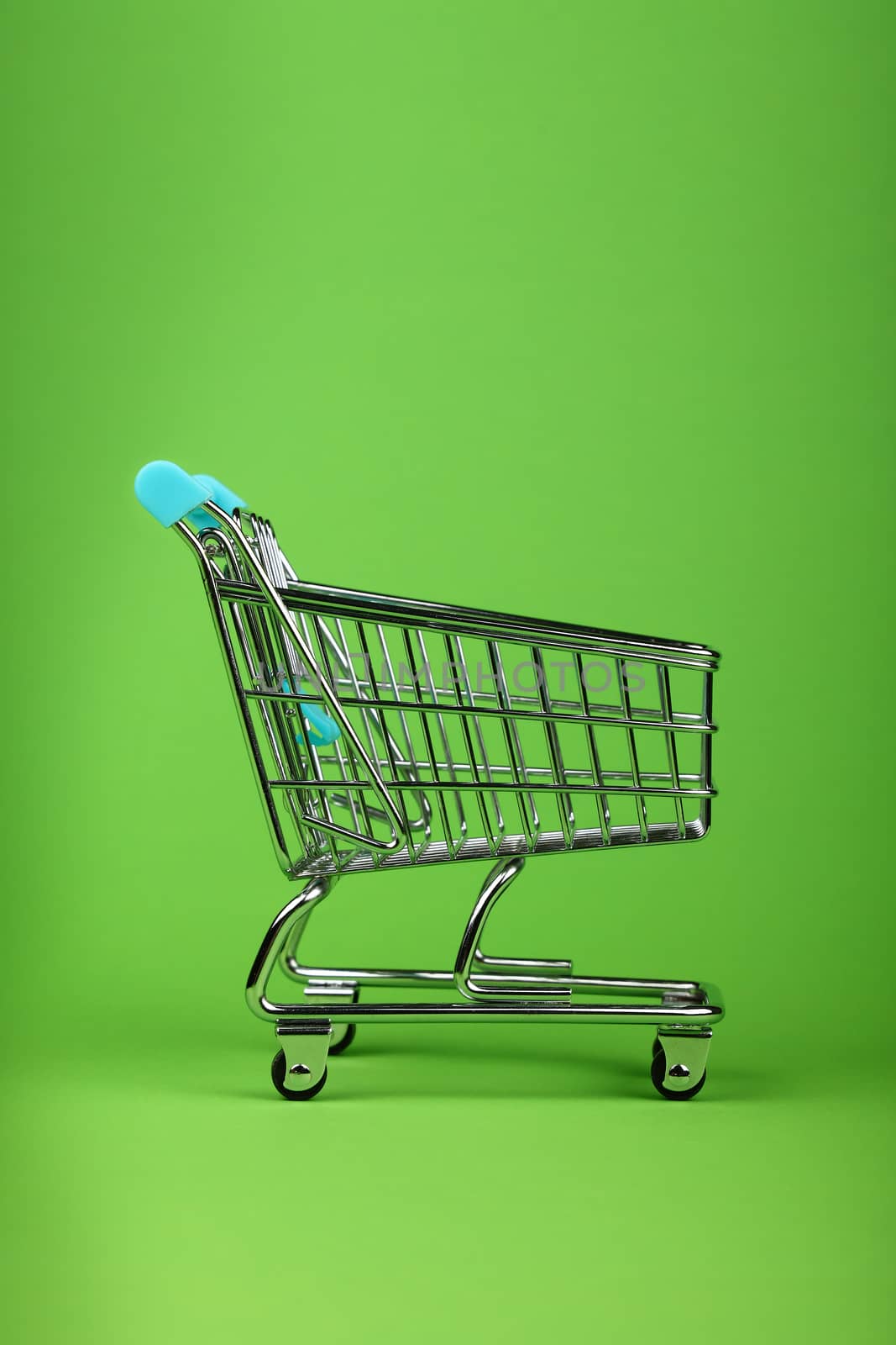 Close up empty toy metal supermarket shopping cart over pastel green background with copy space, low angle side view