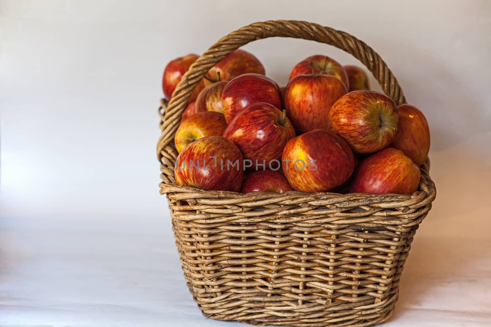 Still life image of a wicker  basket filled with large red Starking apples on a white background.