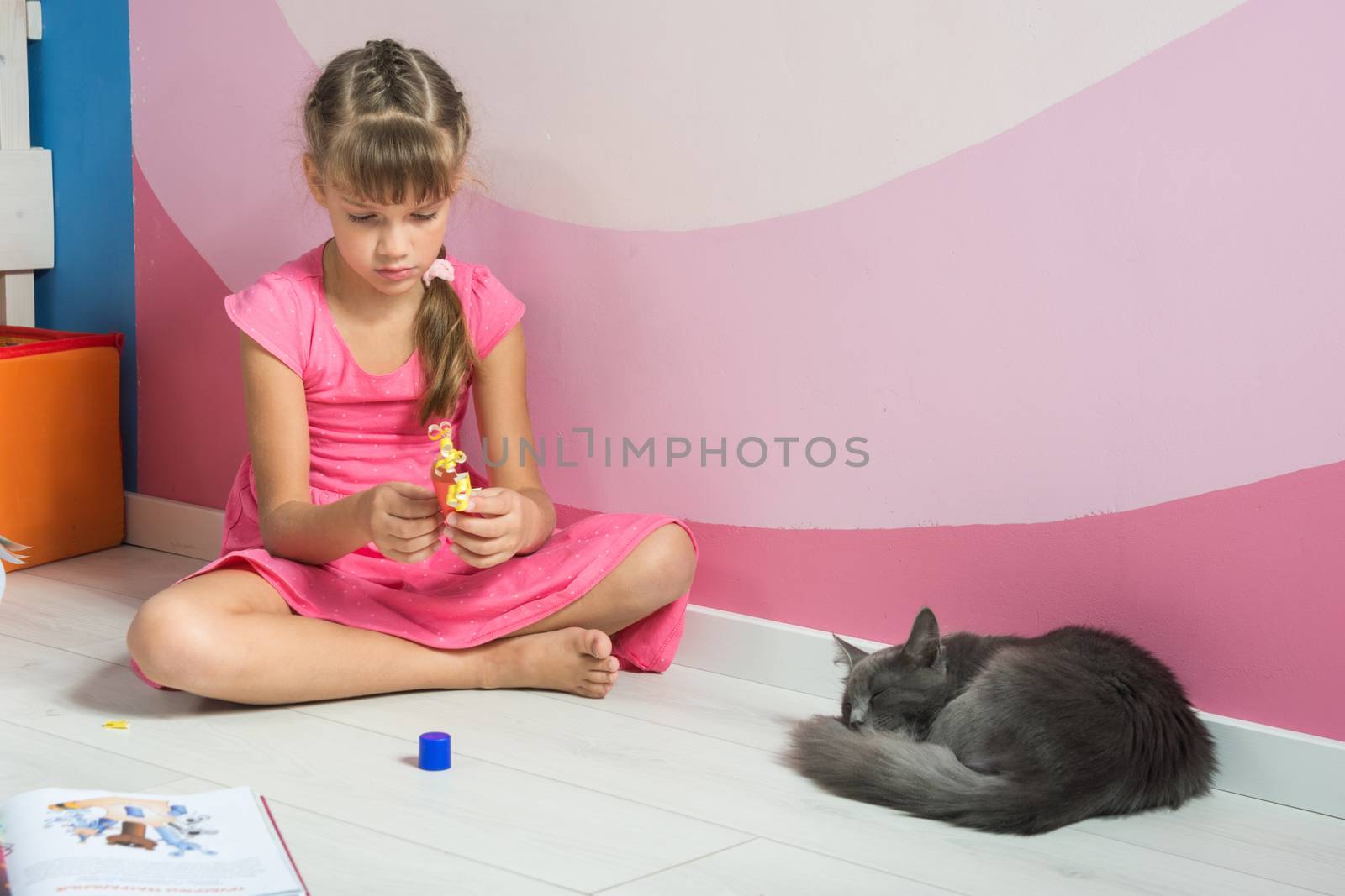 A girl is making figures out of colored paper, a domestic cat is sleeping nearby