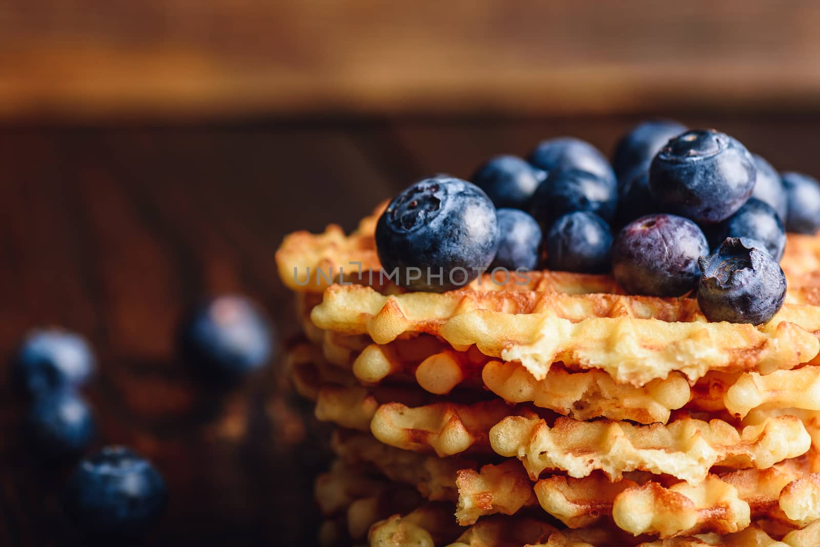 Blueberries on the Top of the Waffles Stack and Other Scattered on Wooden Background.