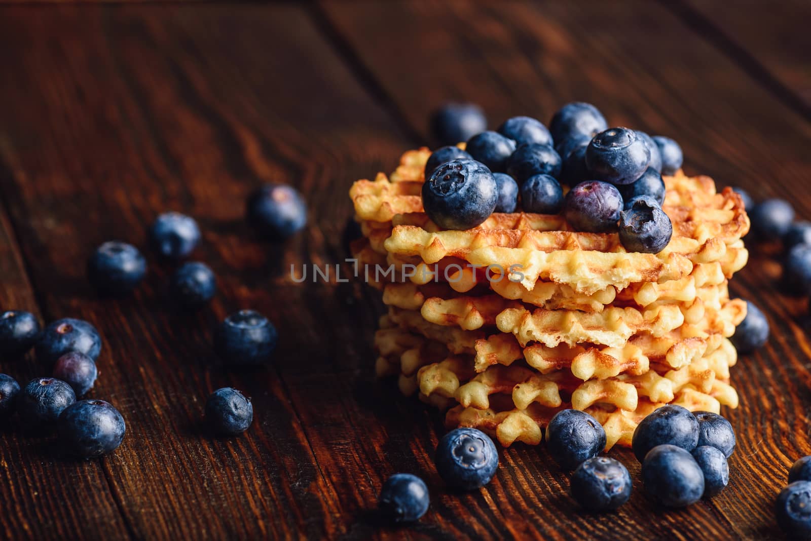 Blueberries on the Top of the Waffles Stack and Other Scattered on Wooden Background. Copy Space on the Left.