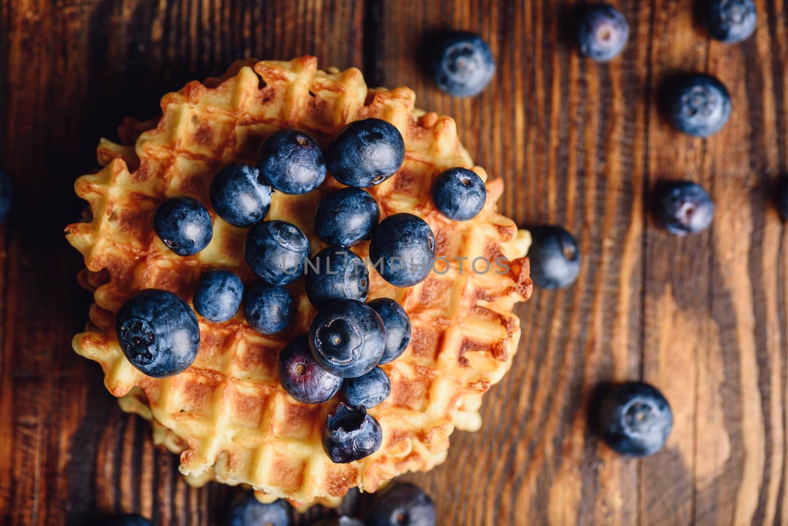 Blueberries on the Top of the Waffle and Other Scattered on Wooden Background. Copy Space on the Right.
