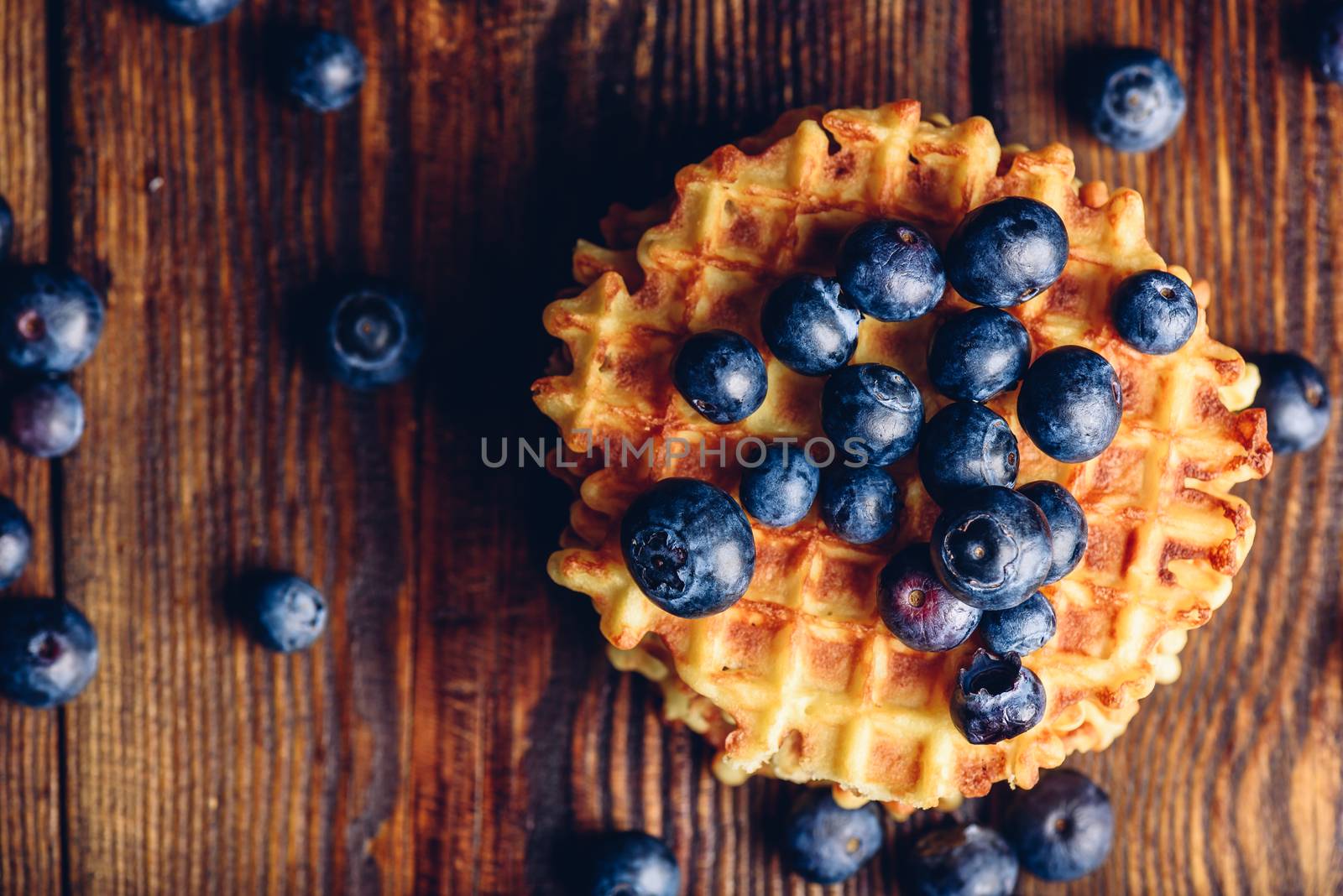 Blueberries on the Top of the Waffle and Other Scattered on Wooden Background. Copy Space on the Left.