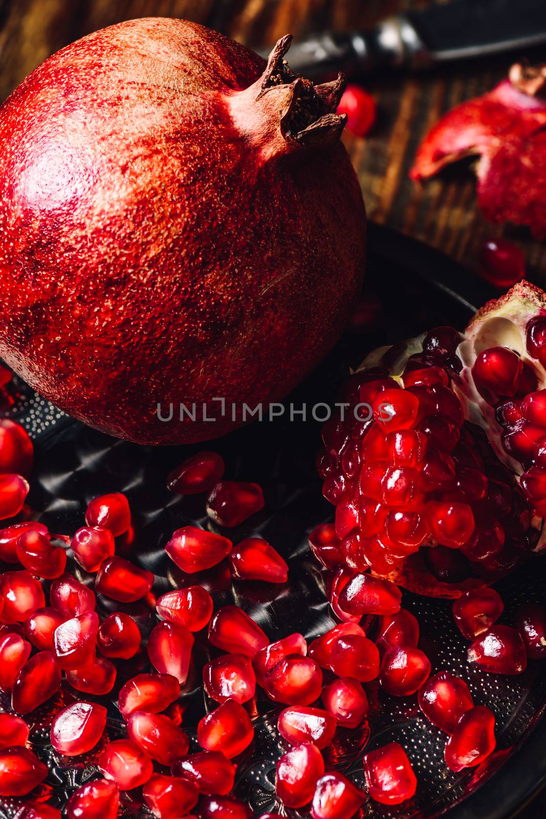 Whole Pomegranate and Opened One wiith Seeds on Metal Plate. Vertical Orientation.