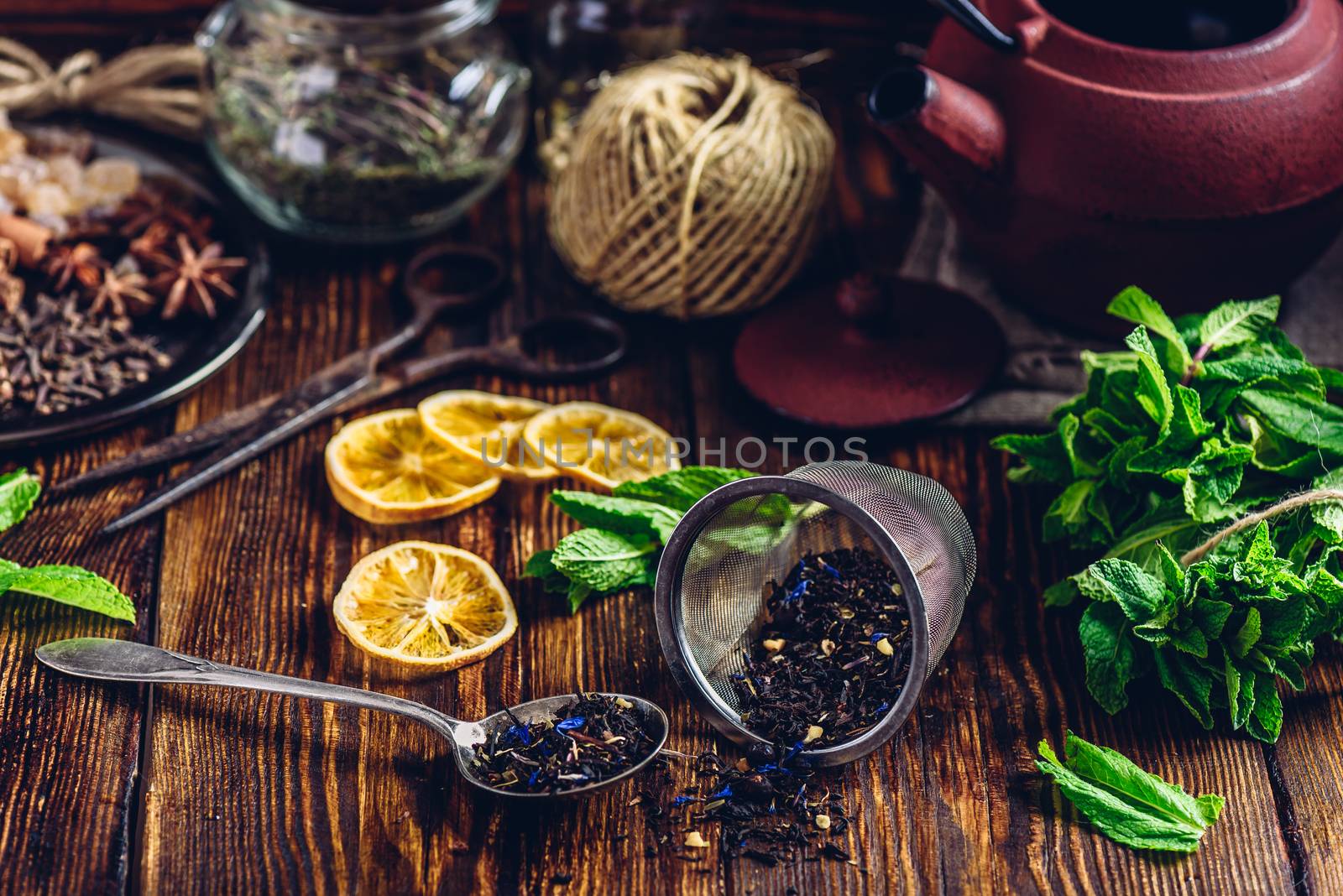 Tea in Strainer and Spoonful of Tea with Fresh Mint, Lemon Slices. Tangle with Two Jars and Teapot on Backdrop.
