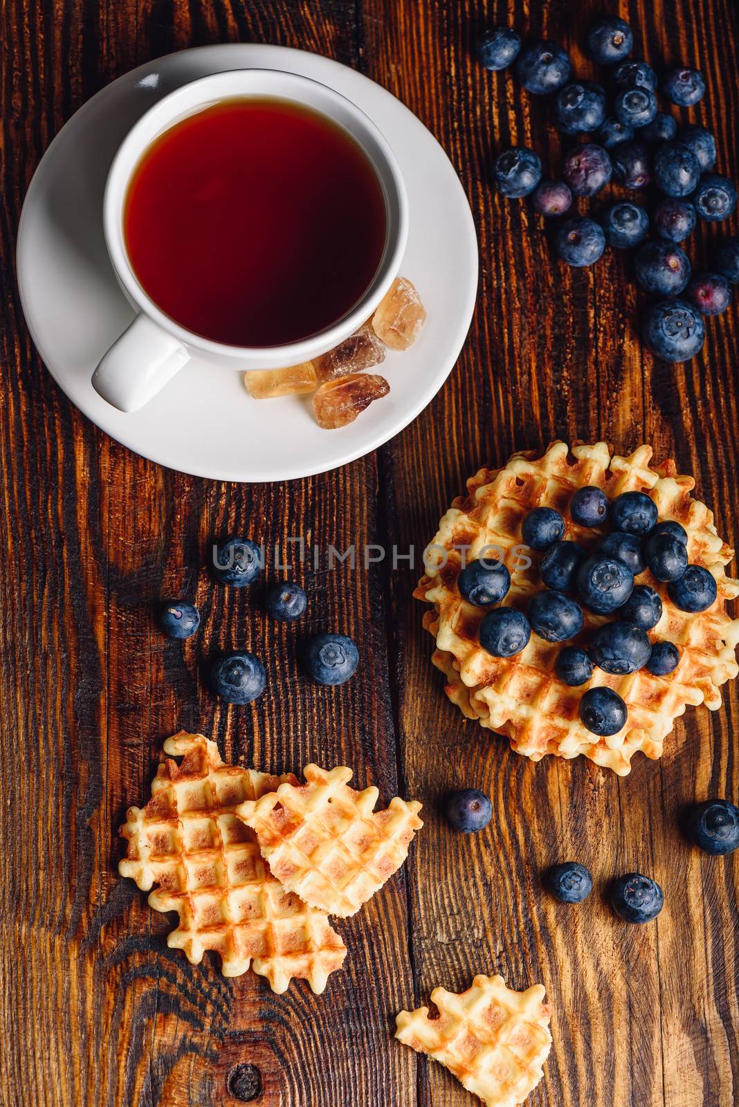 White Cup of Tea with Blueberries and Whole and Broken Belgian Waffles on Wooden Background. Vertical Orientation.