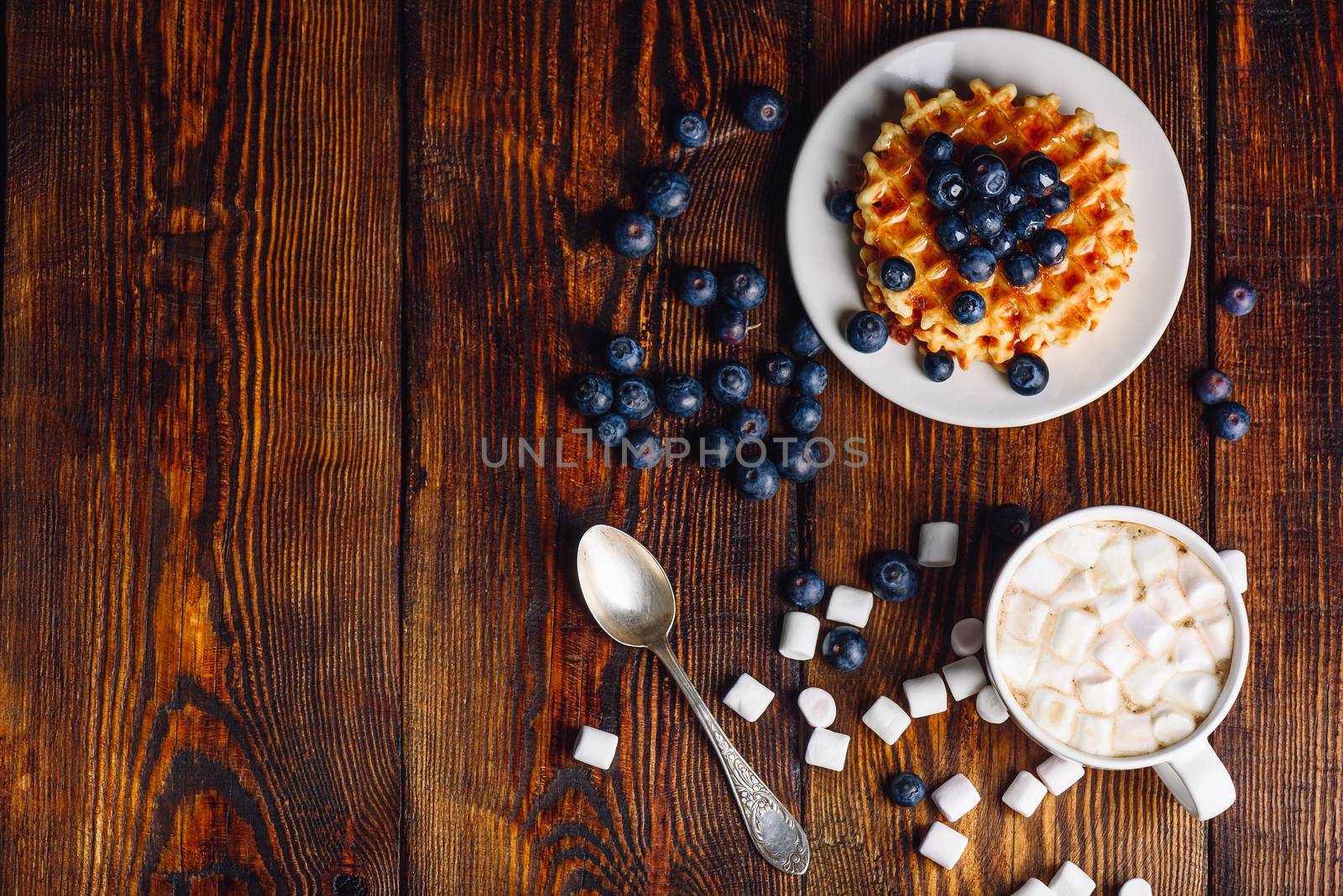 Cup of Hot Chocolate with Marshmallow and Homemade Waffles with Fresh Blueberry and Topping on Plate. Copy Space on the Left. Veiw from Above.