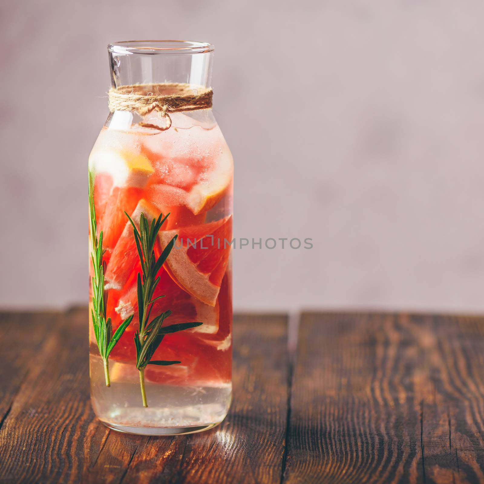 Bottle of Detox Water Infused with Sliced Raw Grapefruit and Fresh Springs of Rosemary. Copy Space on the Right Side.
