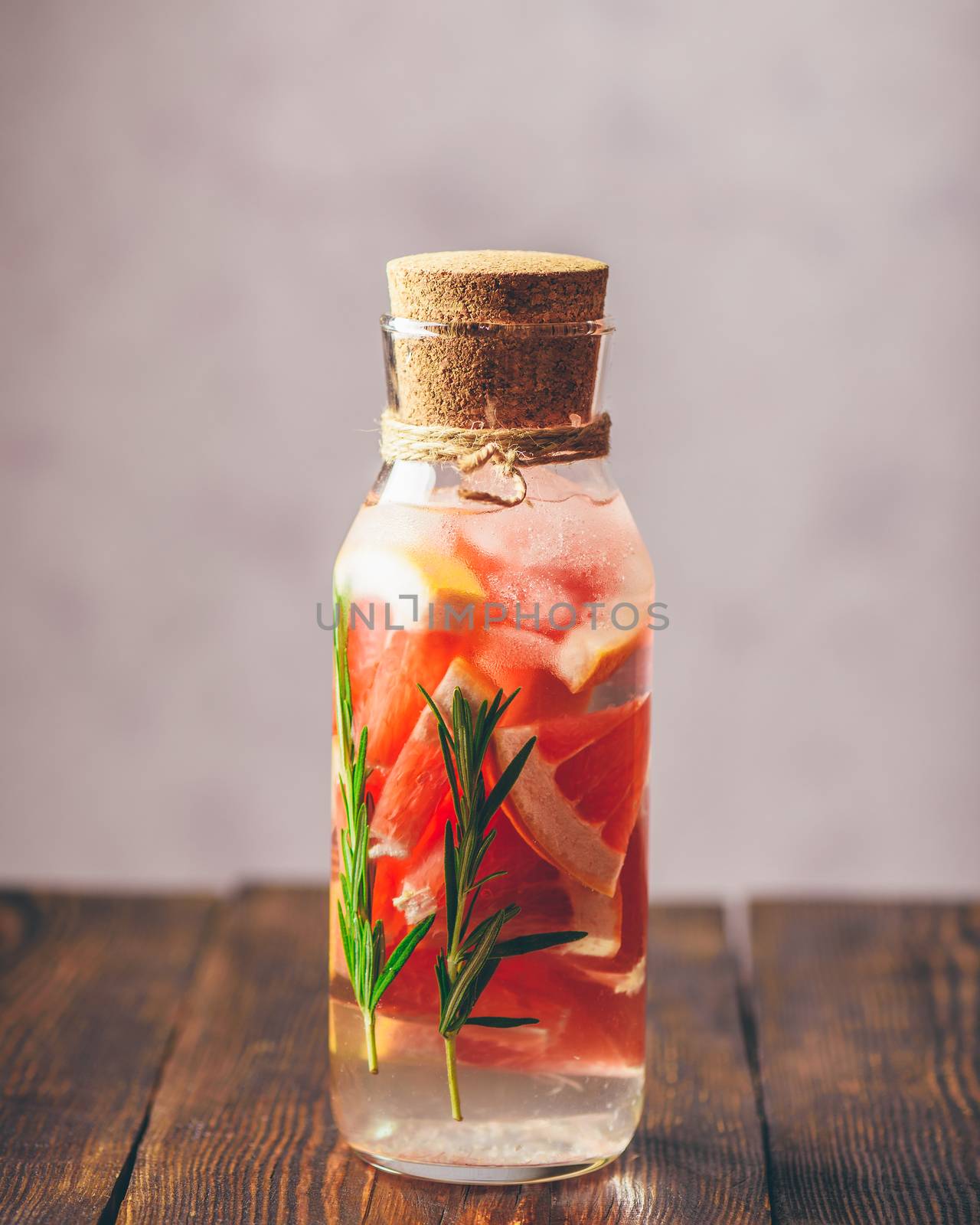 Bottle of Detox Water Infused with Sliced Raw Grapefruit and Fresh Springs of Rosemary. Vertical Orientation. Copy Space on the Top.